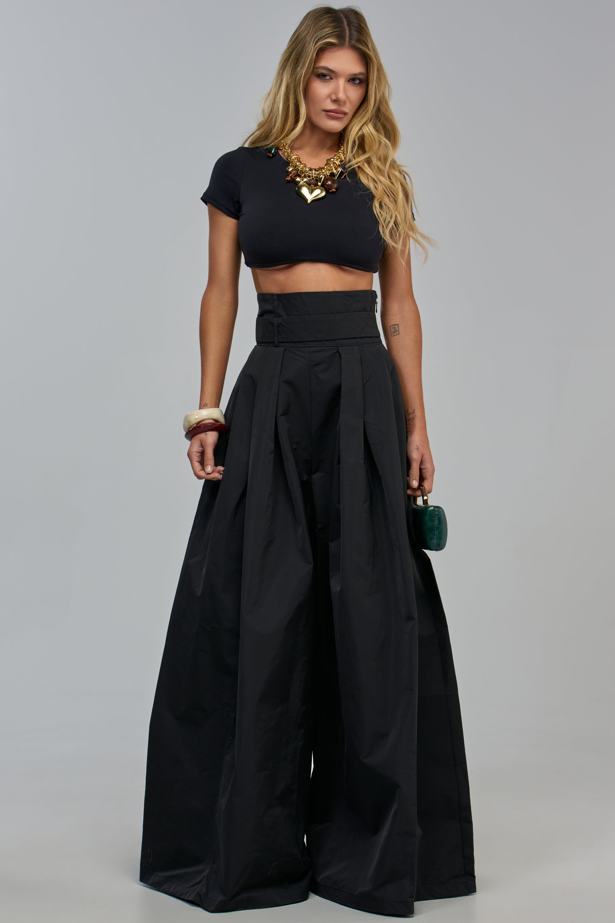A woman wears a black cropped t-shirt and PAIGE PLEATED PANT high-rise, wide-leg pleated pants.