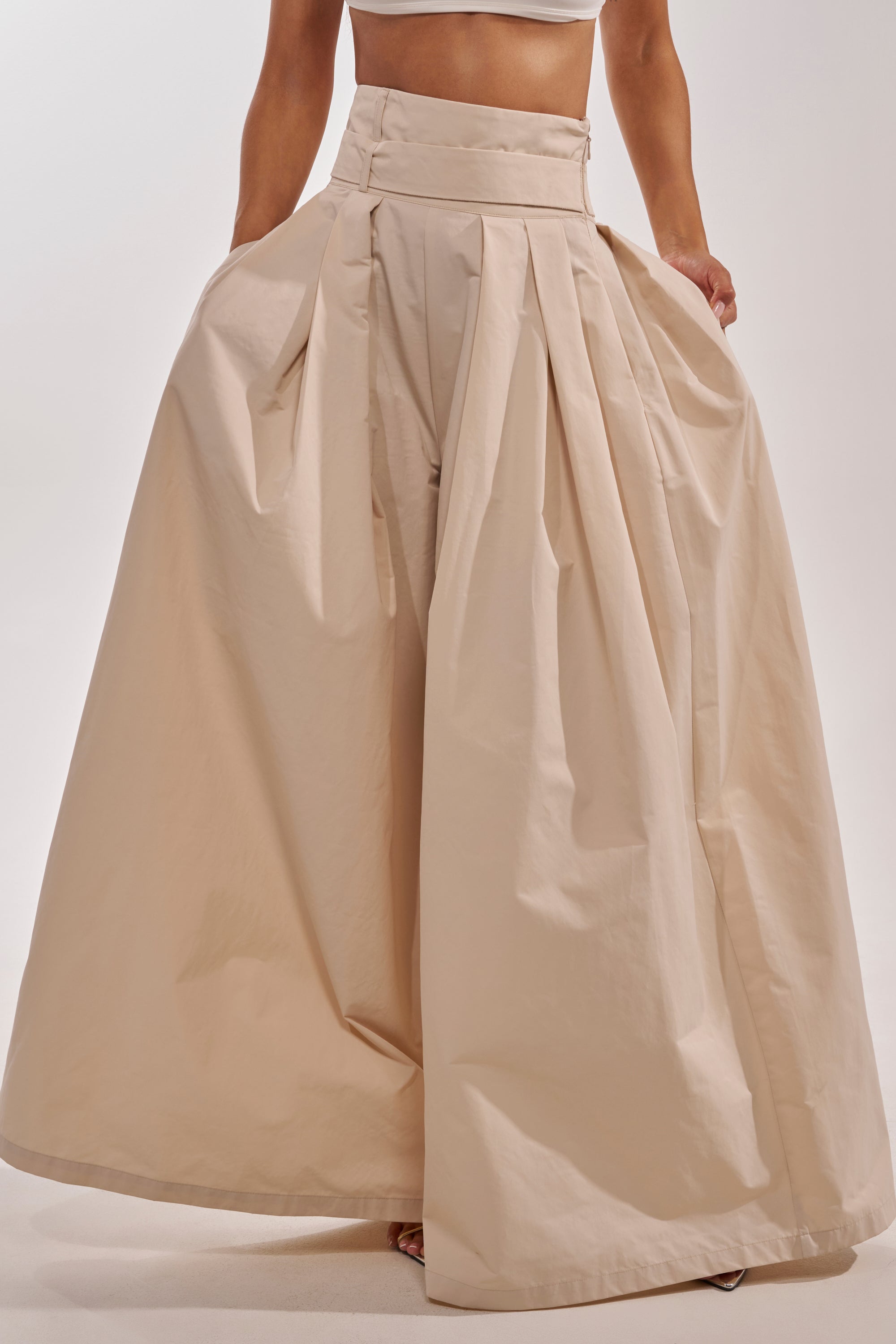Wearing the DISCO DOLL TROUSER—beige high-rise, wide-leg pants with pleats and a floor-length, skirt-like silhouette—paired with a cropped top against a plain light background. 1