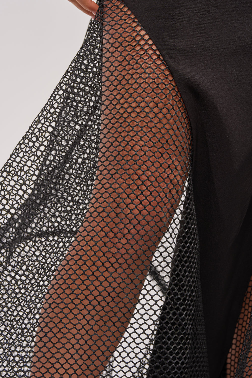 Close-up of a person wearing the FREE IN MOTION MAXI SKIRT, a black mesh maxi skirt layered over a black outfit. The sheer mesh fabric reveals skin and highlights the bold texture and pattern of this statement evening piece. 7