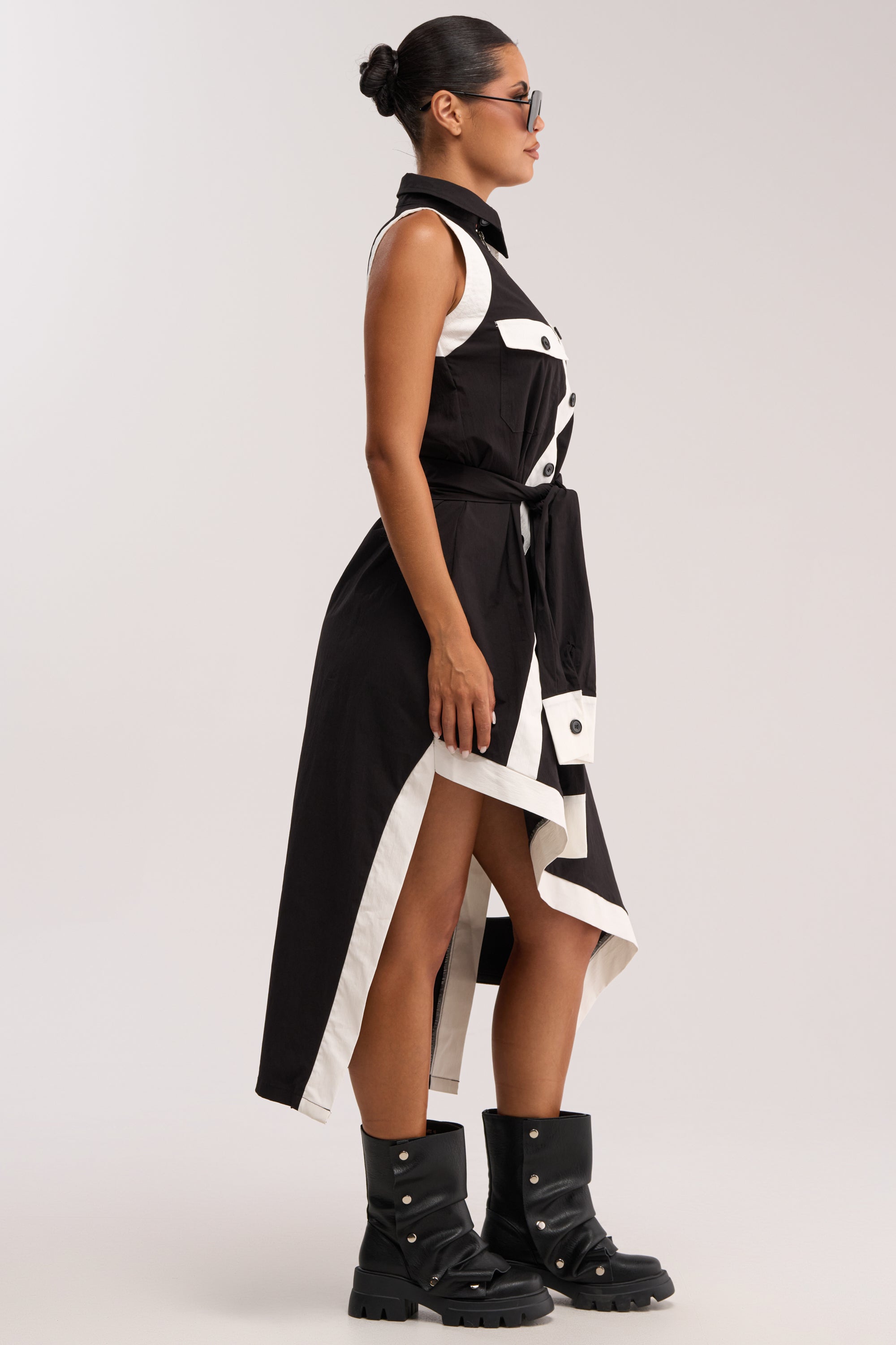 A woman in profile wears sunglasses and the NO FILTER NEEDED BUTTON UP MAXI DRESS, a sleeveless black-and-white colorblock design with button details and a tie belt, paired with chunky black boots featuring metallic accents.