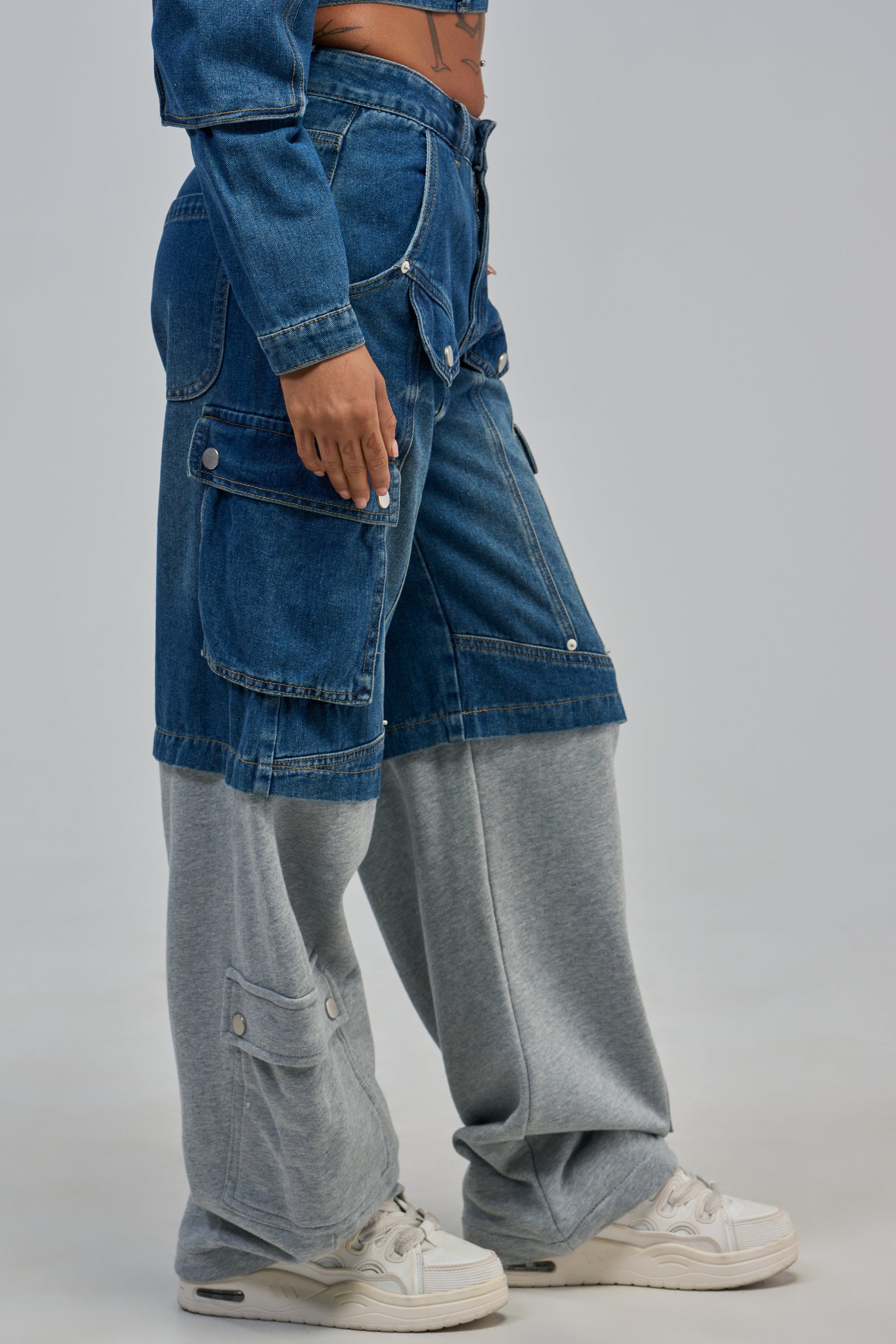 A person wearing THE IT GIRL DENIM PANT over gray sweatpants with white sneakers stands against a plain background.