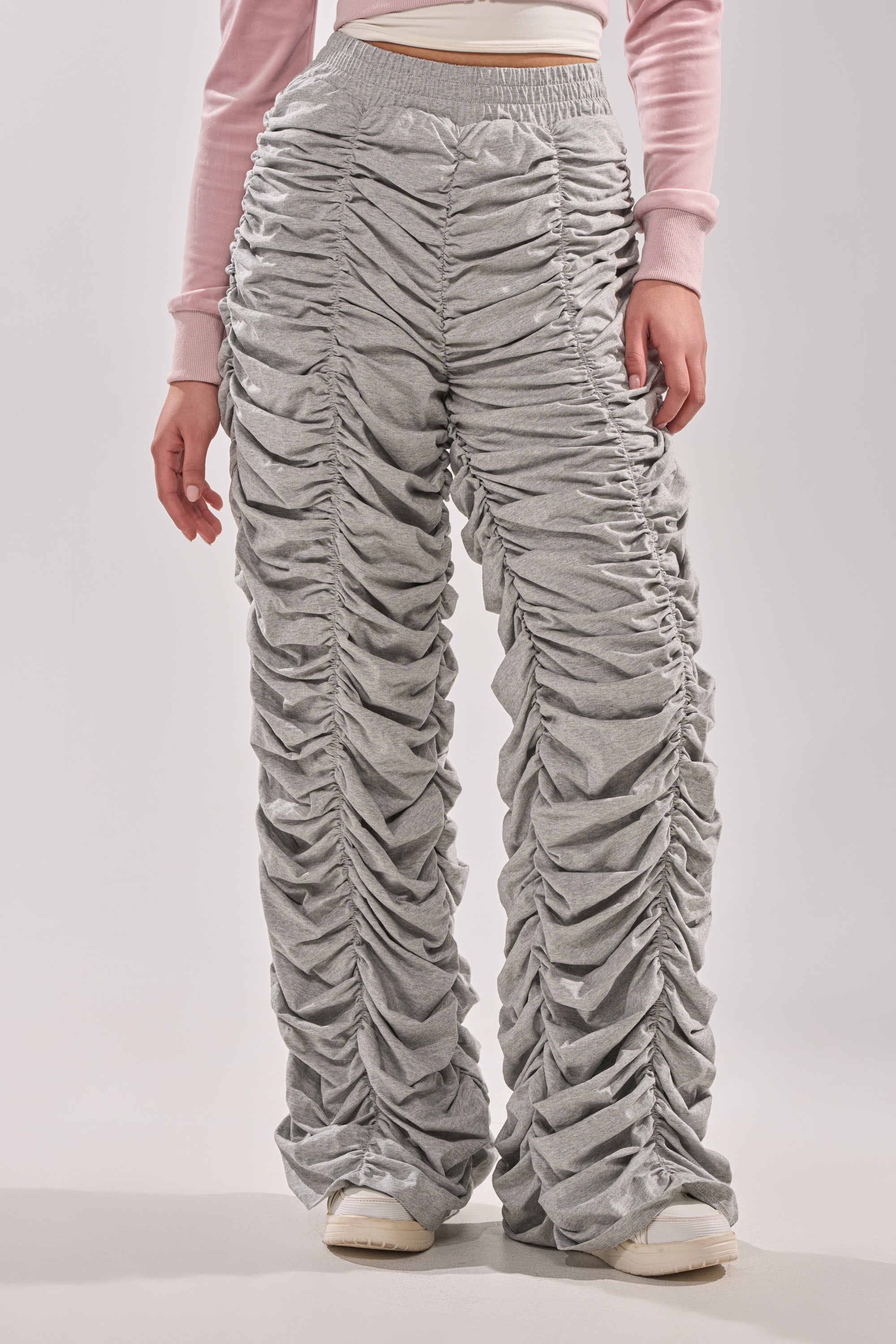 Wearing the IM THAT TYPE RUCHED JOGGER in heather grey with a light pink long-sleeve crop top and white sneakers, the lower half of the person is shown against a plain background. 1