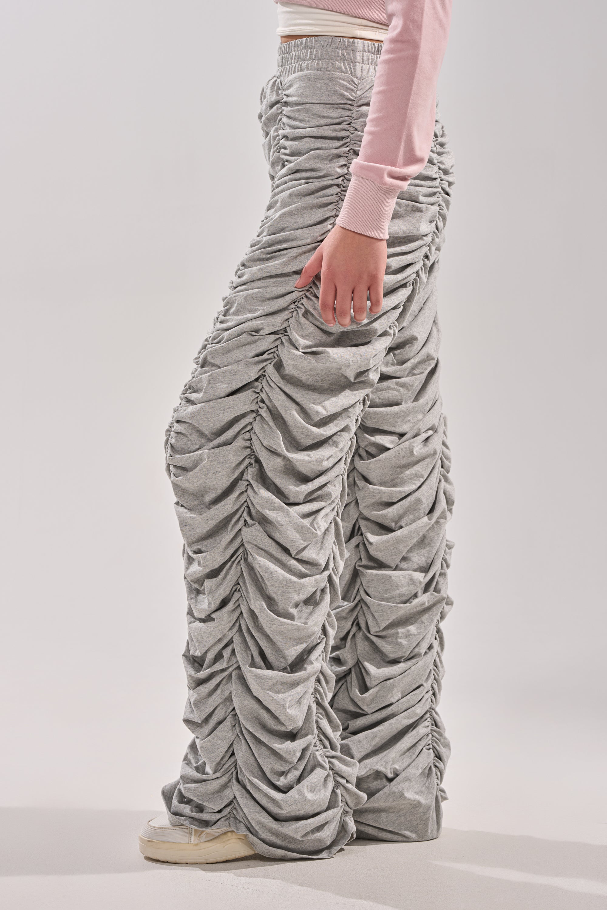 Wearing the IM THAT TYPE RUCHED JOGGER in light gray, paired with a pale pink long-sleeve top and white sneakers, a person stands against a plain light background. 2