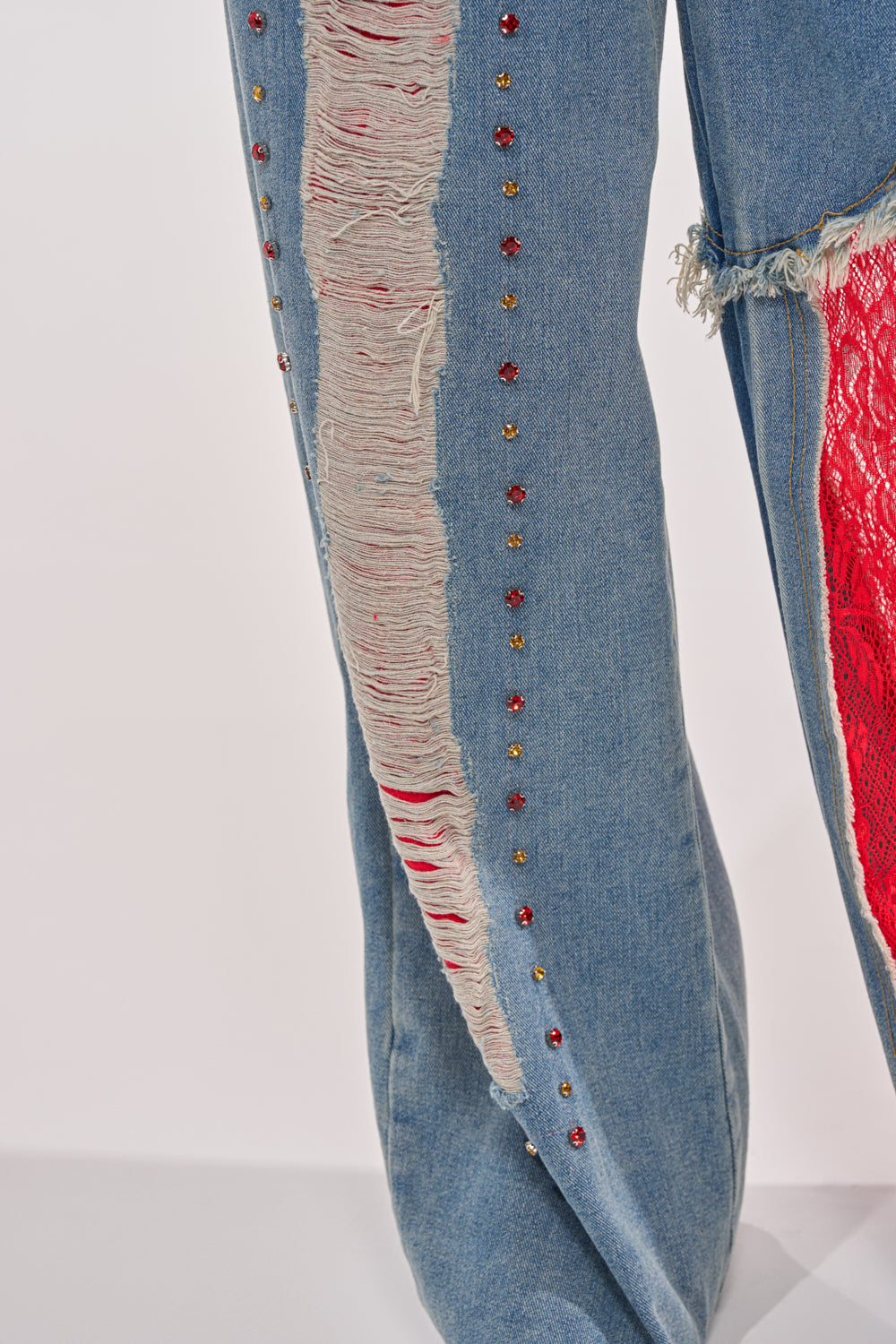 Close-up of the GAME TIME JOGGER blue denim jeans with a large distressed tear, frayed edges, red fabric underneath, and decorative red and gold studs—ideal for making a bold streetwear statement in your patchwork jogger collection. 7