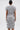 A person faces away from the camera in the TIED DOWN KNOT MIDI DRESS, a fitted, hand-tied knot cotton dress in gray. The knee-length style is styled with a neat bun, hoop earrings, and bracelets for a chic look.