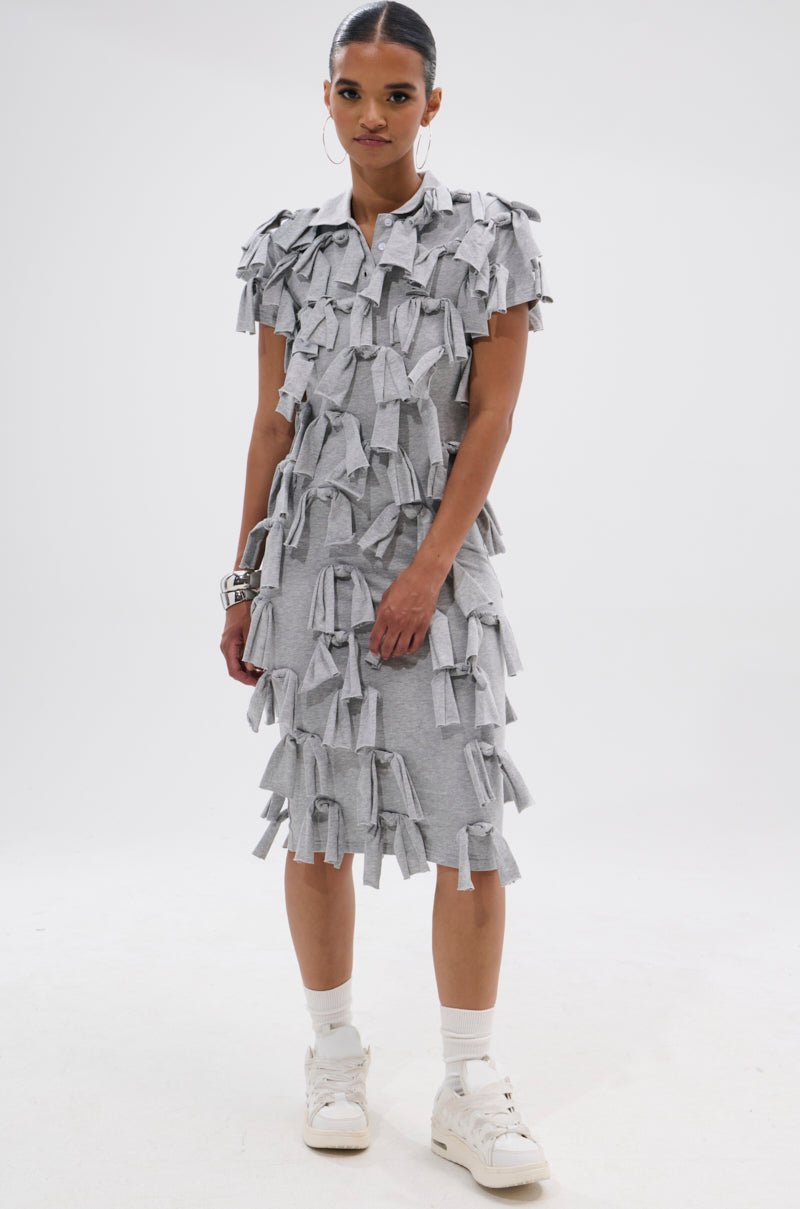 A woman wears the TIED DOWN KNOT MIDI DRESS in light gray, featuring hand-tied knots, styled with white sneakers, socks, and silver bracelets, standing against a plain white background.