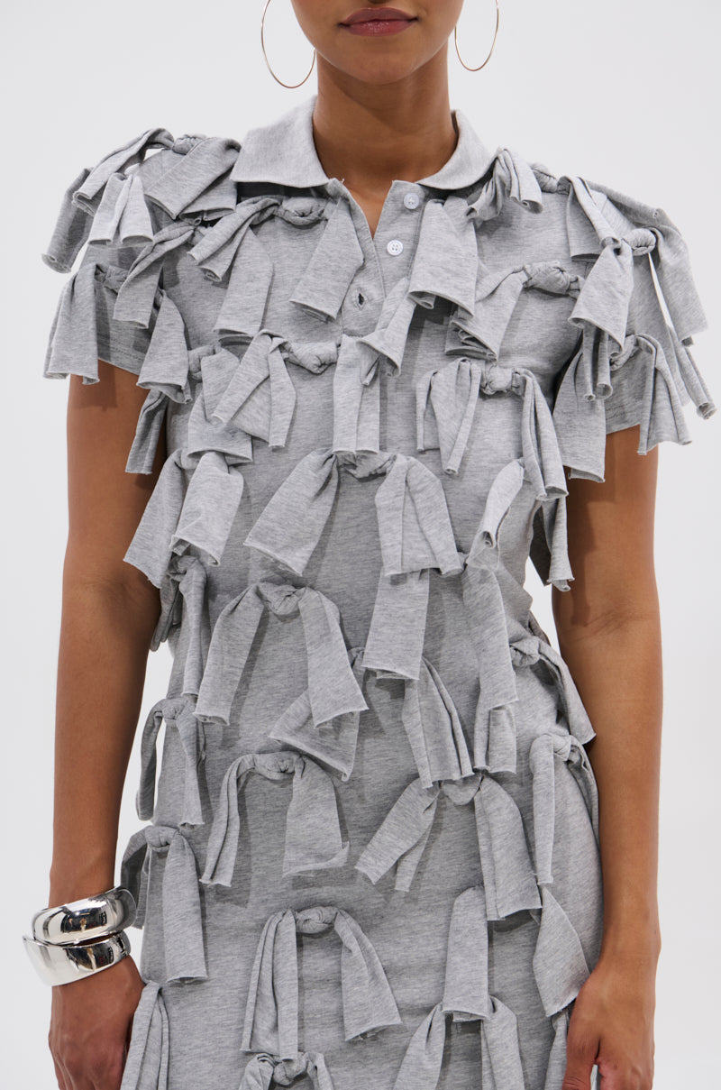 A woman models the TIED DOWN KNOT MIDI DRESS in light gray cotton with hand-tied knots, styled with silver hoop earrings and a chunky bracelet, against a plain white background. Her face is partially out of frame.