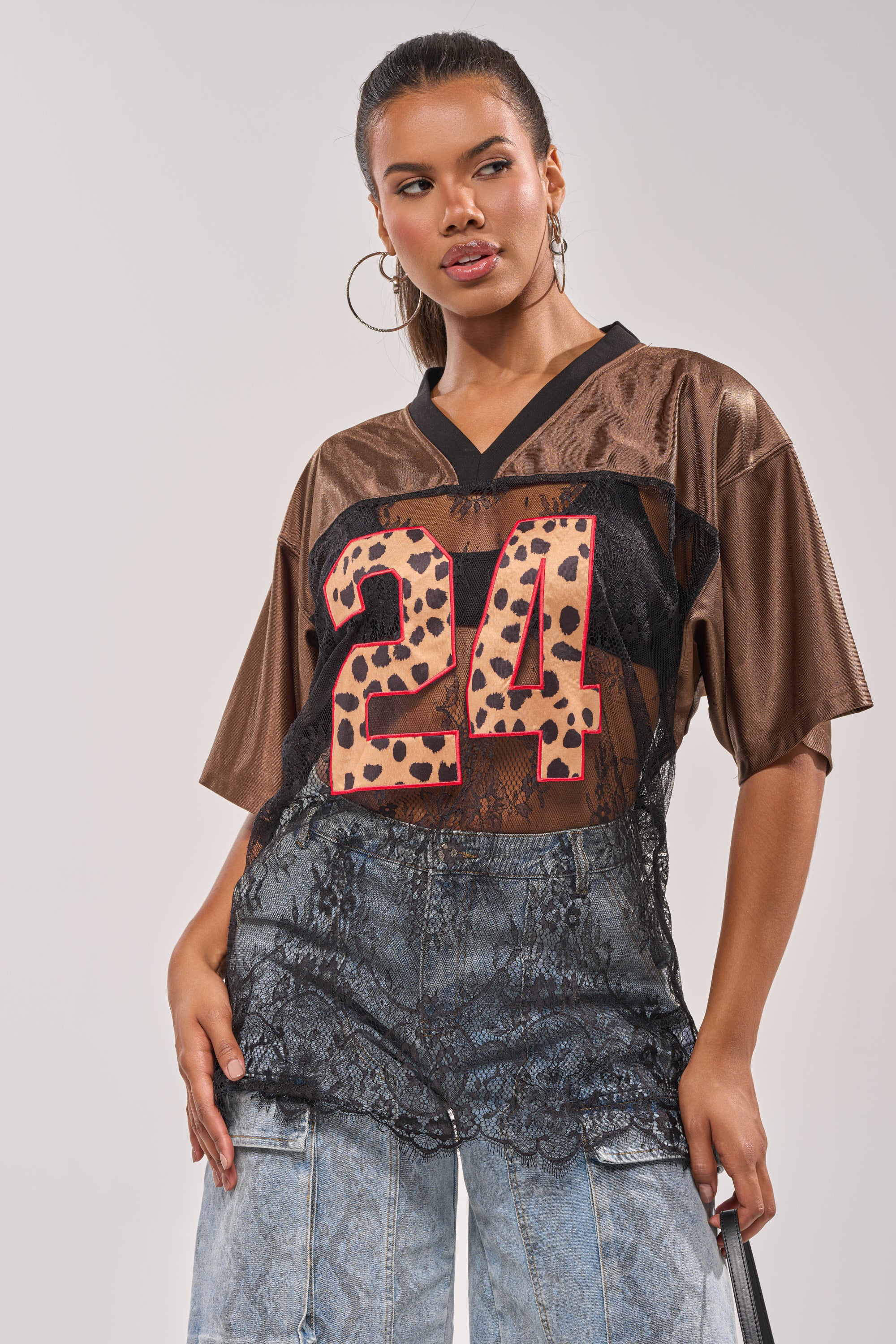 A woman sports the LUCKY 24 JERSEY—an oversized top with a sheer lace panel and bold leopard-print "24"—styled over light blue patterned jeans, hoop earrings, and her hair pulled back for a street-chic vibe. 4