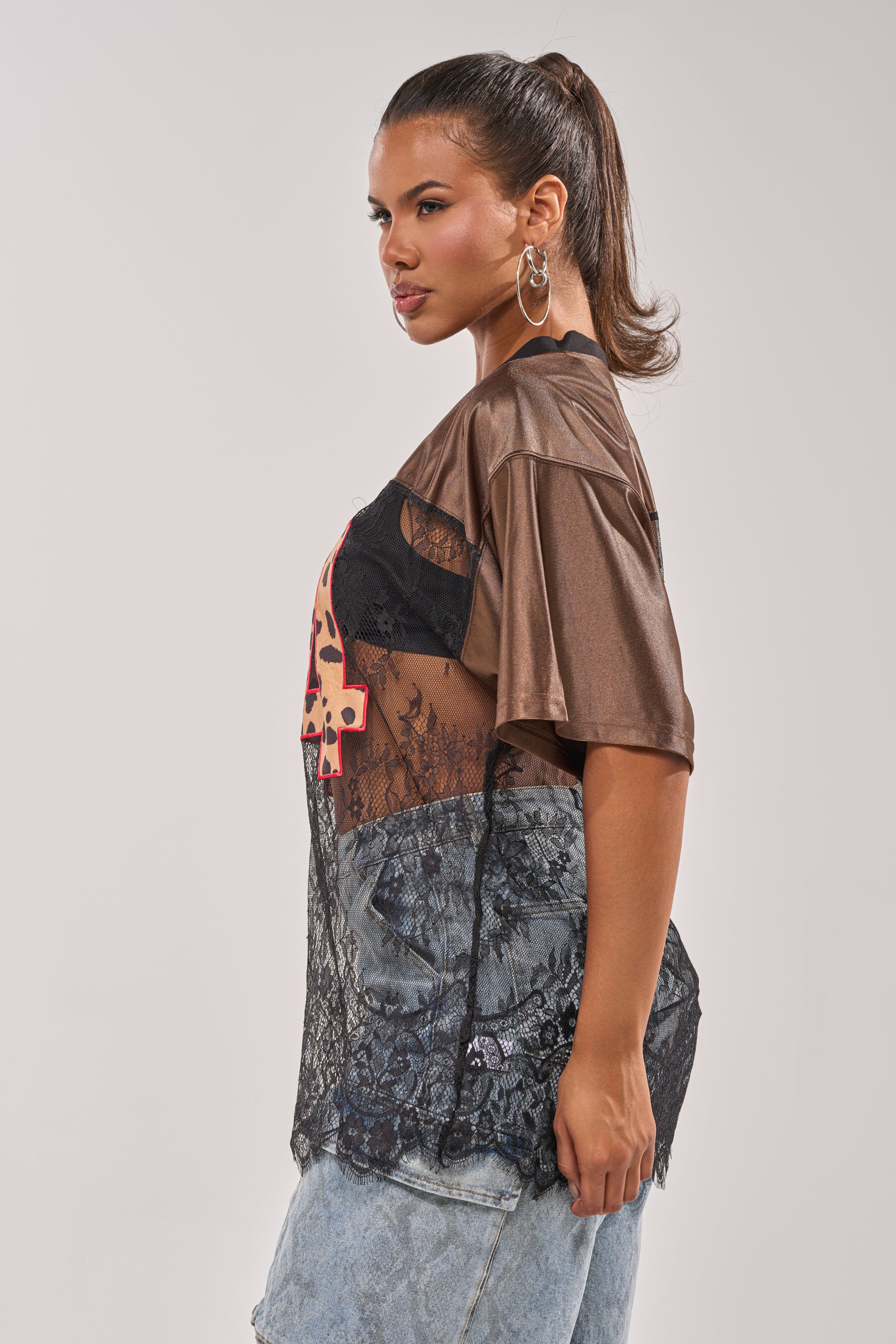 Wearing the LUCKY 24 JERSEY, a woman in profile layers it over a black sheer lace panel with light-wash jeans. She channels street-chic style with hoop earrings and a high ponytail, gazing ahead against a simple background. 5