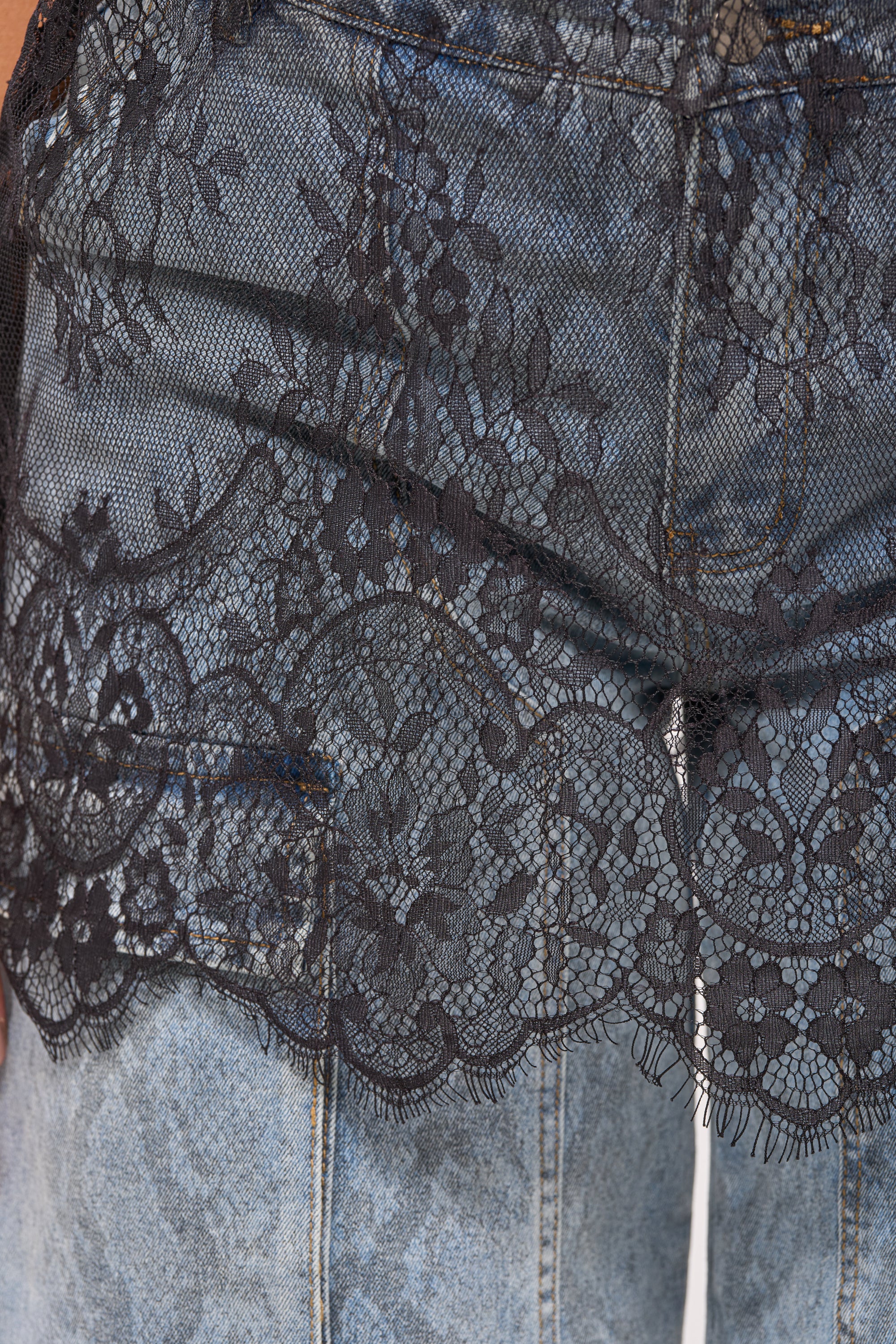Close-up of the LUCKY 24 JERSEY blue denim jeans, featuring a sheer lace panel overlay with black floral designs delicately covering the upper portion. 10