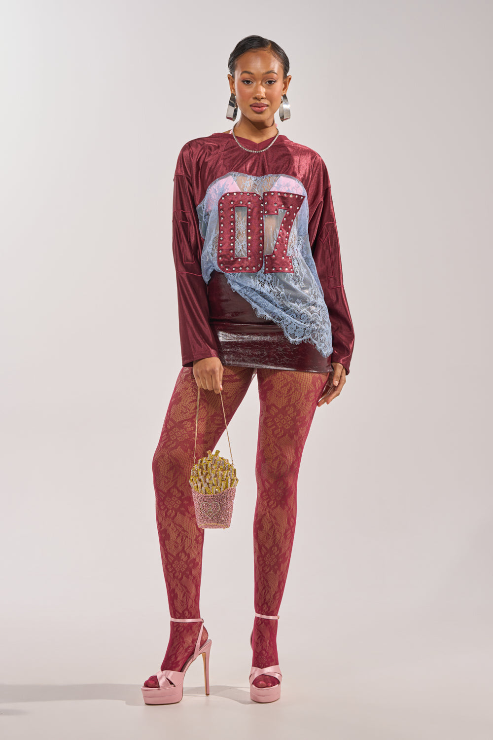 A woman stands confidently in the sporty-chic WINNER JERSEY featuring “07” on the front, paired with red lace tights, pink platform heels, large earrings, and holding a rhinestone bucket with faux French fries. 6