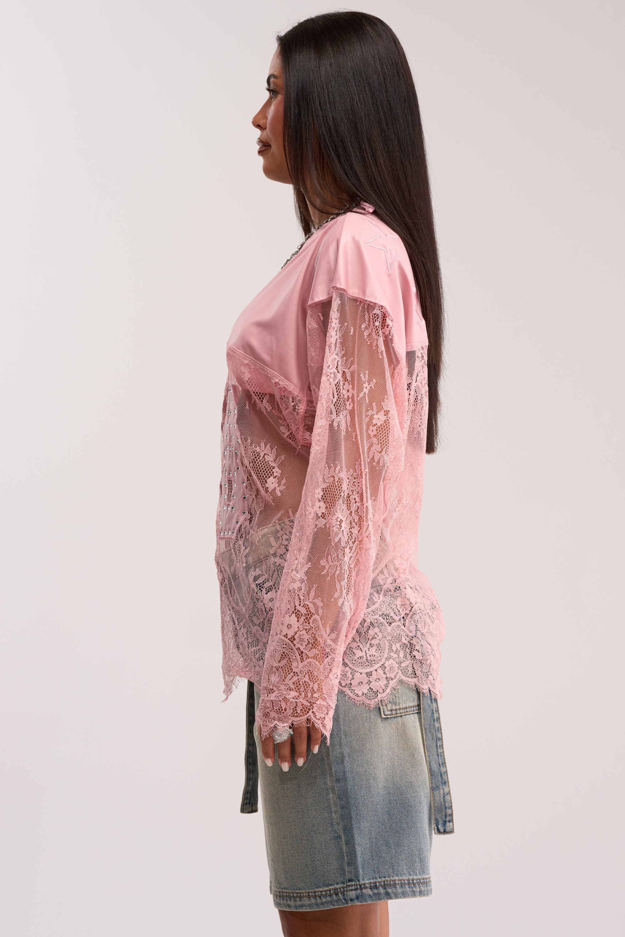 A woman in profile wears the GIRLS ARE PLAYERS TOO LACE JERSEY TOP over a sporty top and knee-length denim skirt, with straight dark hair and arms at her sides, set against a plain background.