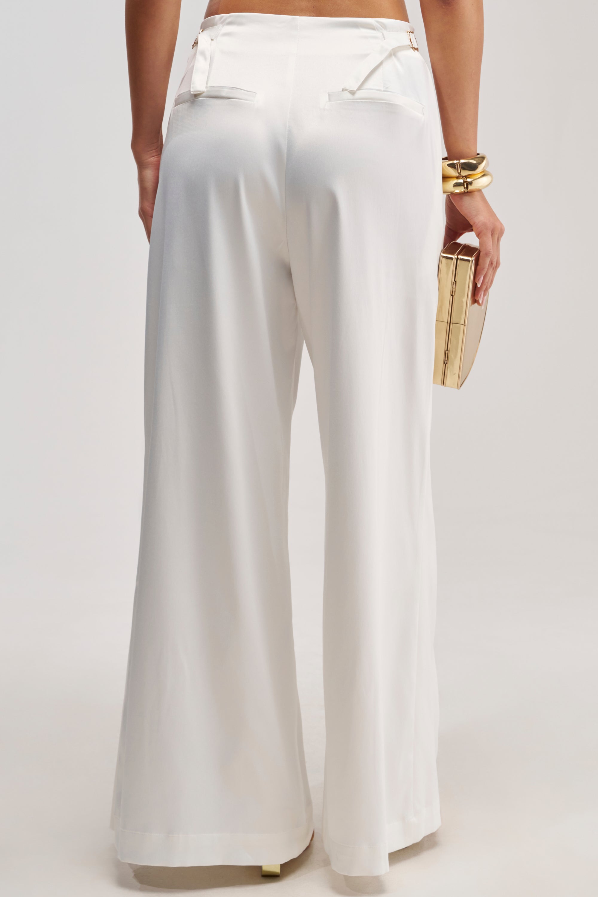 A person is shown from the back against a plain background, wearing the WHITE PARTY EMBELLISHED RELAXED PANT styled with gold bangles and a boxy gold clutch—the perfect ensemble for modern bridal pants styling inspiration.