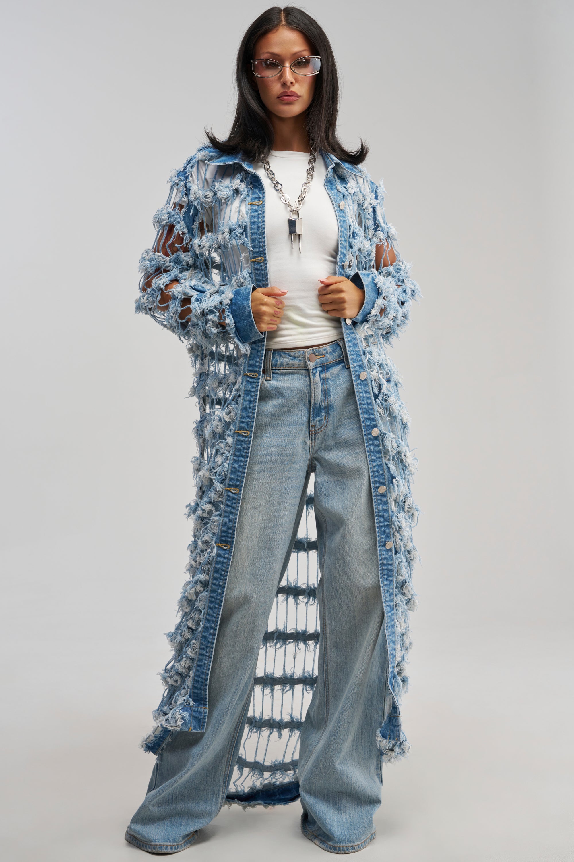 A woman wearing glasses, a white shirt, wide-leg jeans, and the GOOD TIME NOT A LONG TIME DENIM TRENCH stands confidently against a plain light background—a striking example of modern streetwear style.
