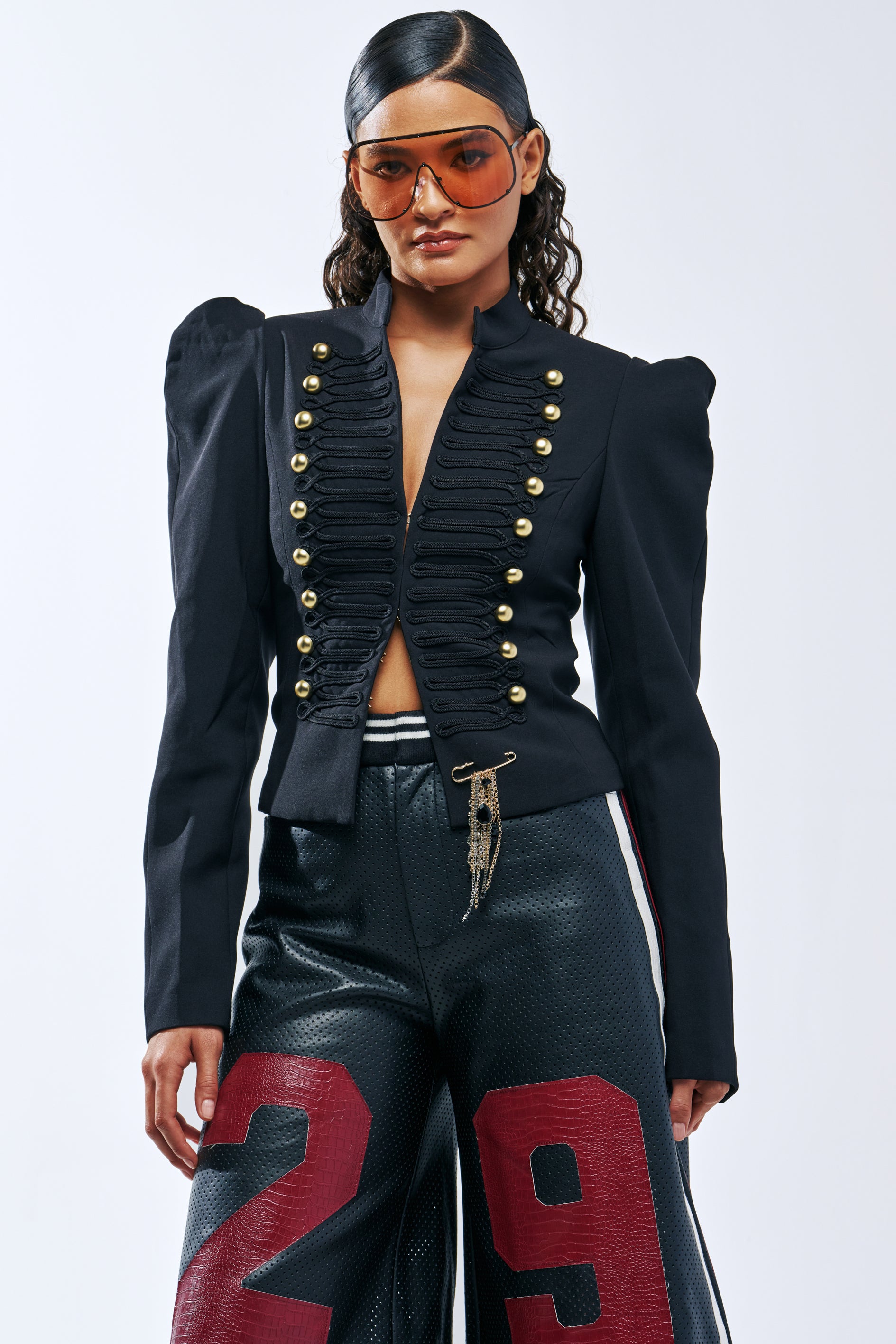 A person wears a black SINCLAIR PUFF SHOULDER BLAZER with gold buttons over dark, textured pants with large red numbers on the legs.