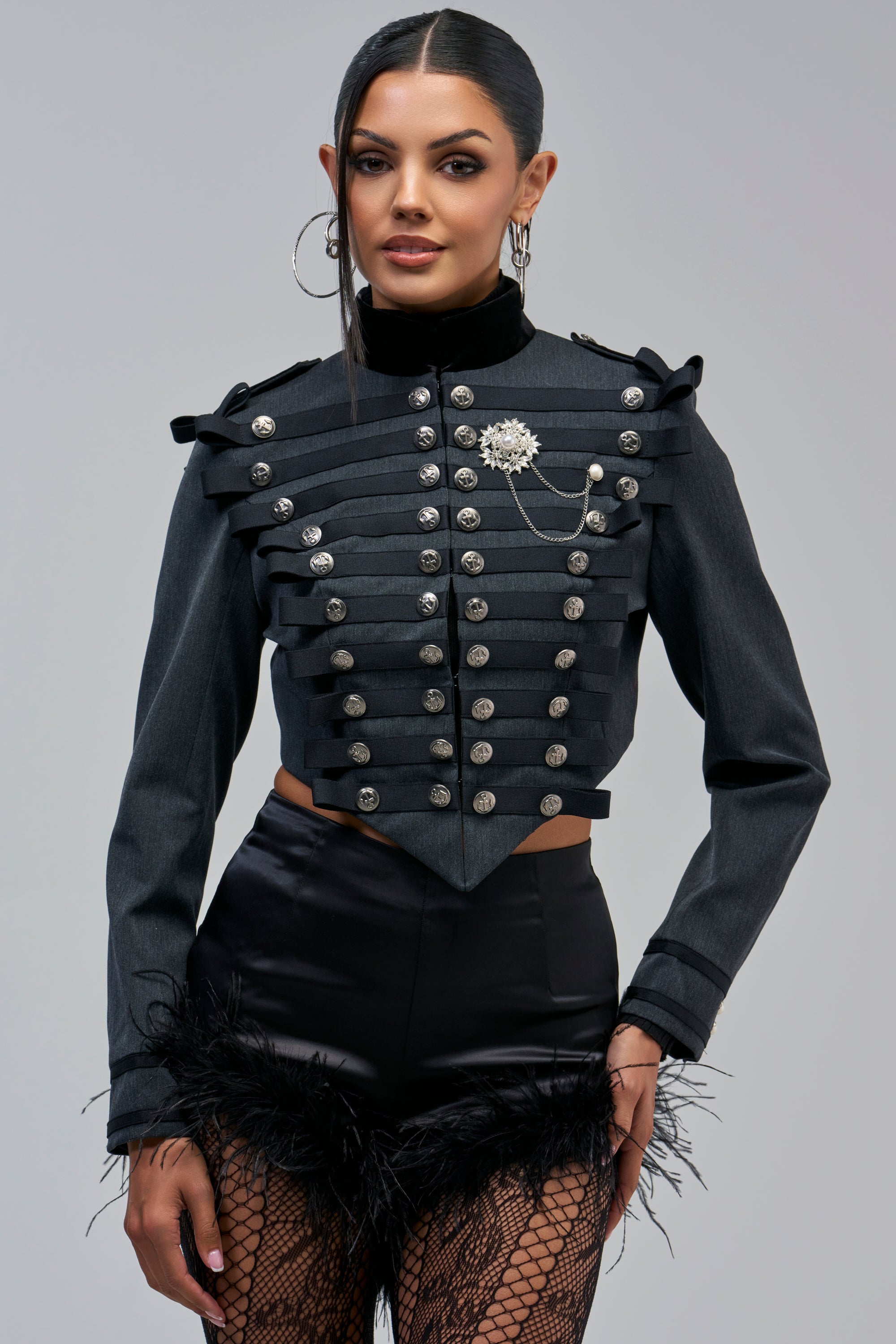 A cropped grey CADET BLAZER with silver buttons, black ribbon trim, and a decorative brooch with a chain.