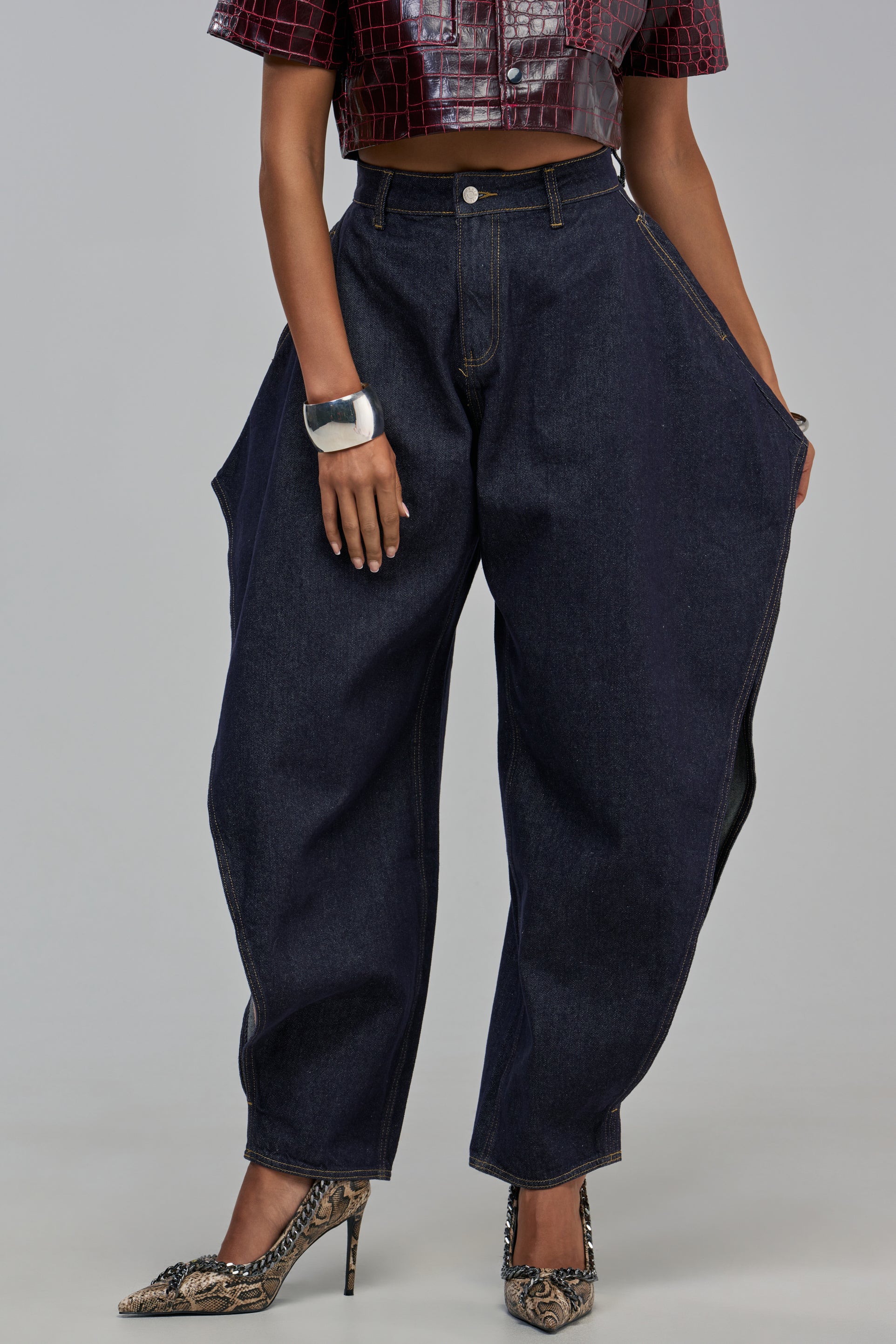 CARLY CUT OUT JEAN in dark wash denim with wide, curved legs and hip cutouts, styled with a dark red cropped top and snakeskin-print pointed-toe heels.