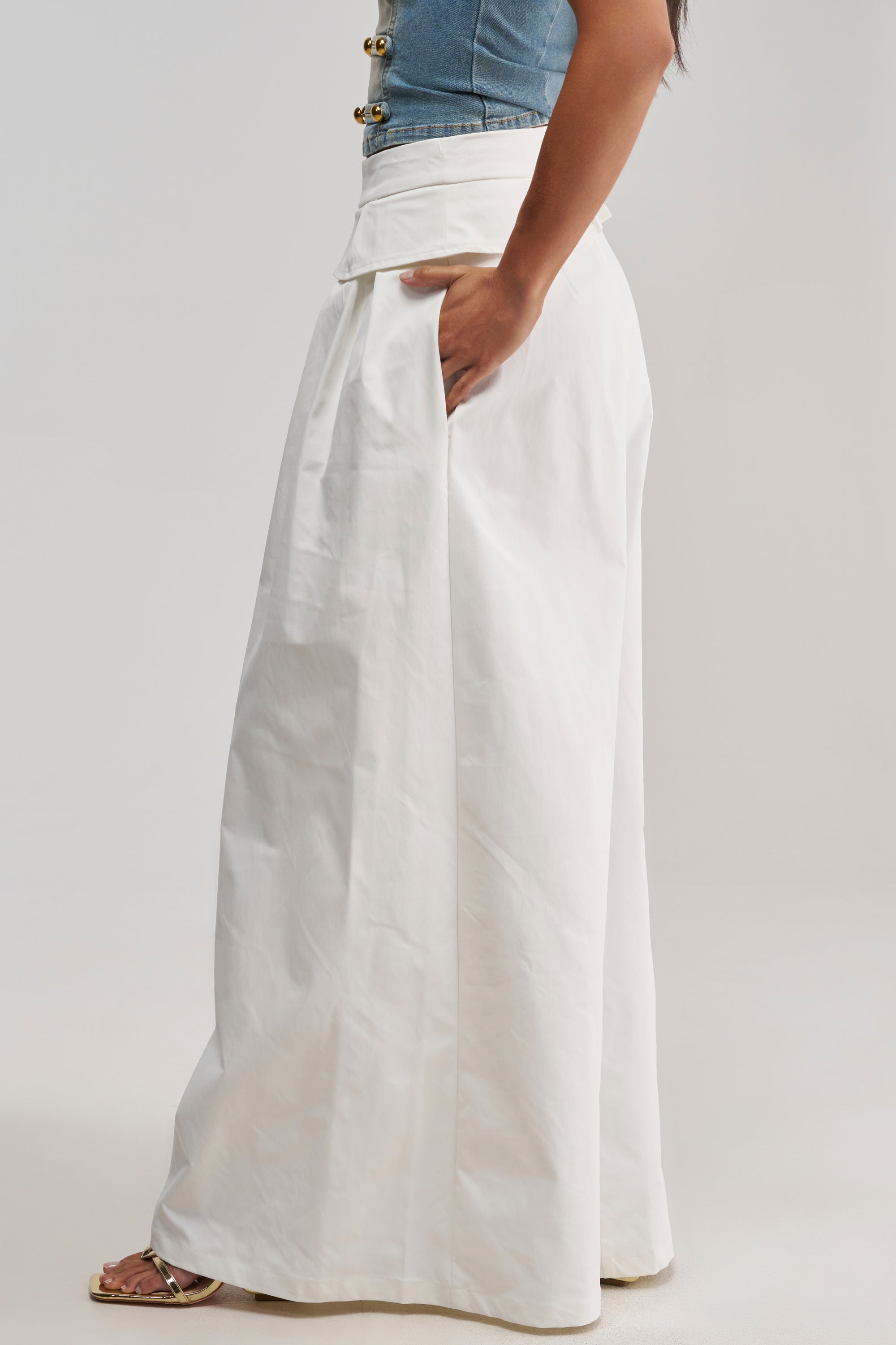 A person wearing the LOCKED IN LOVE TROUSER in white stands sideways with one hand in the pocket, showcasing only the lower body.