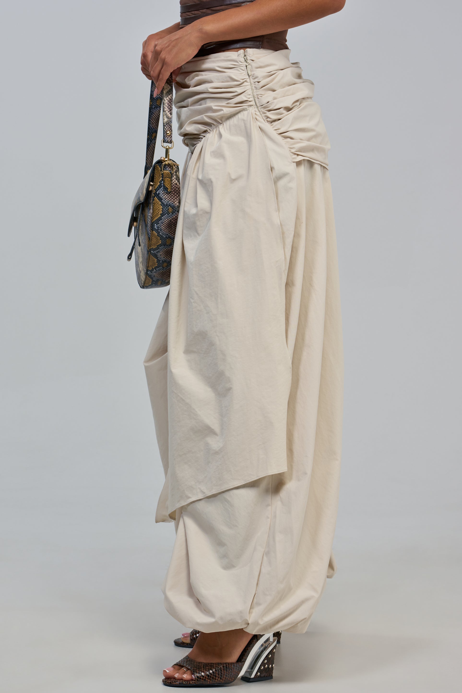 A person wearing the NOT MY TYPE TROUSER—a pair of loose, cream-colored balloon trousers crafted from soft beige fabric—and holding a patterned handbag. Only the lower body is visible against a plain, light background.