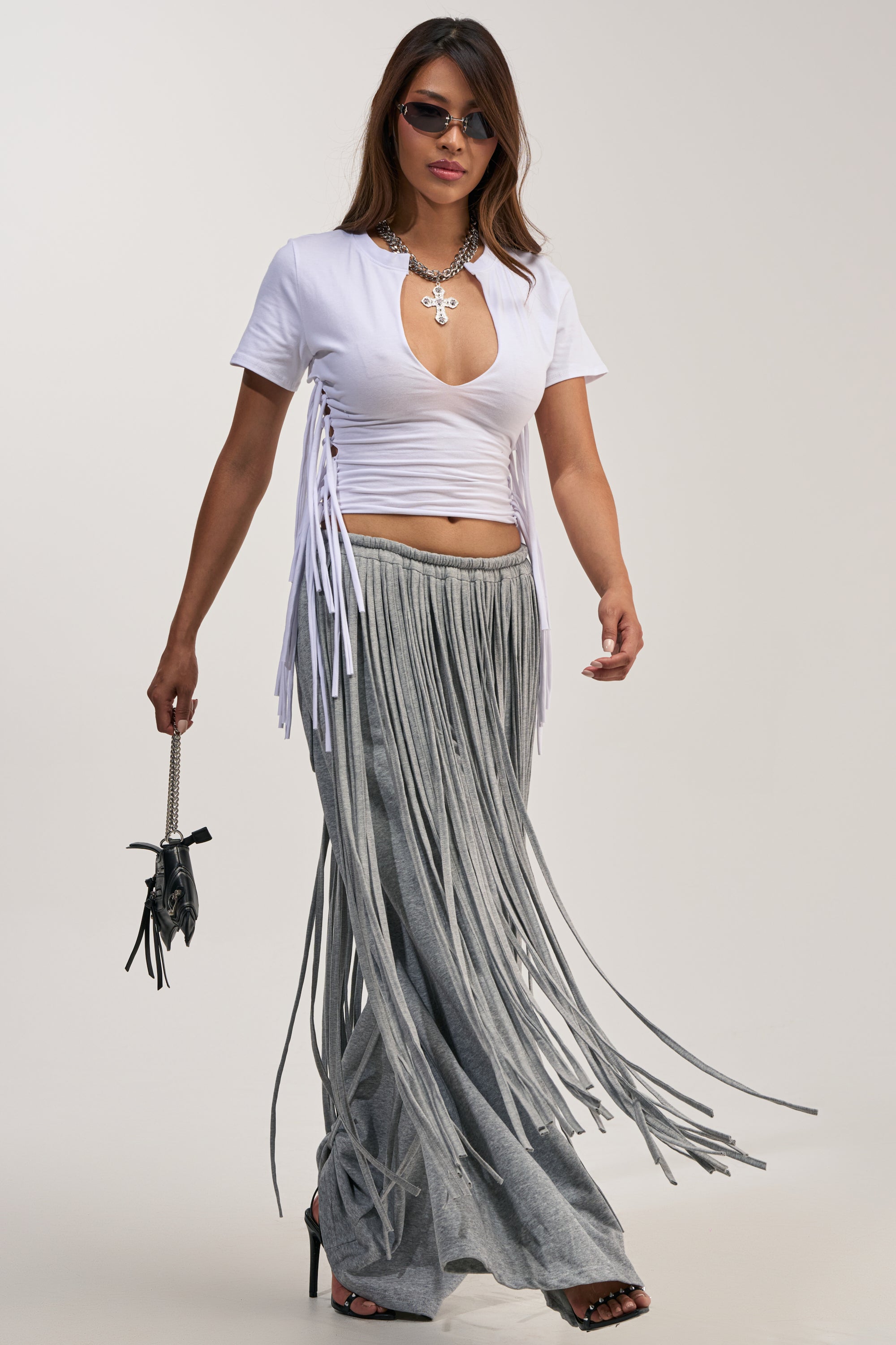 A woman in sunglasses wears a white ruched cutout top, the TRY ME FRINGE WIDE LEG JOGGER in gray, black heels, and carries a small black handbag.