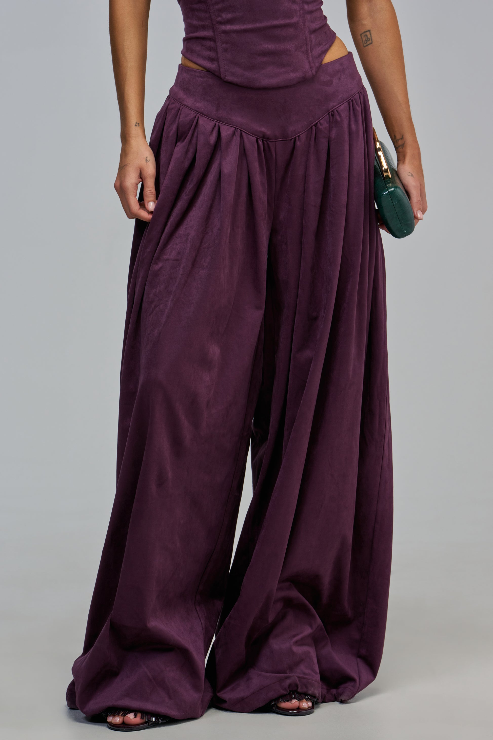 A person wearing DARK PLUM SUEDE BALLOON PANT in a high-rise fit and a matching corset-style top.