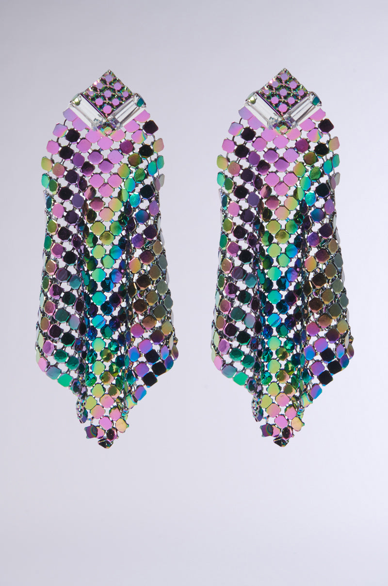 The ON THE DANCE FLOOR EARRING showcases a vibrant hexagonal pattern with colorful, reflective elements that create an iridescent effect against a light gray background. Its intricate design, accented with gemstones, features a lively blend of greens, purples, blues, and pinks.