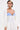 Wearing the COVER UP CHIFFON SHRUG—billowy white chiffon sleeves—over a strapless blue-and-white pinstriped corset with gold buttons and white pants, a person with short dark hair and a blonde streak stands out against a white background.