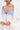 Wearing the COVER UP CHIFFON SHRUG, a sheer white piece with billowy sleeves and a blue-and-white striped, buttoned bodice, this person’s chest and finger tattoos pop against the plain white backdrop.