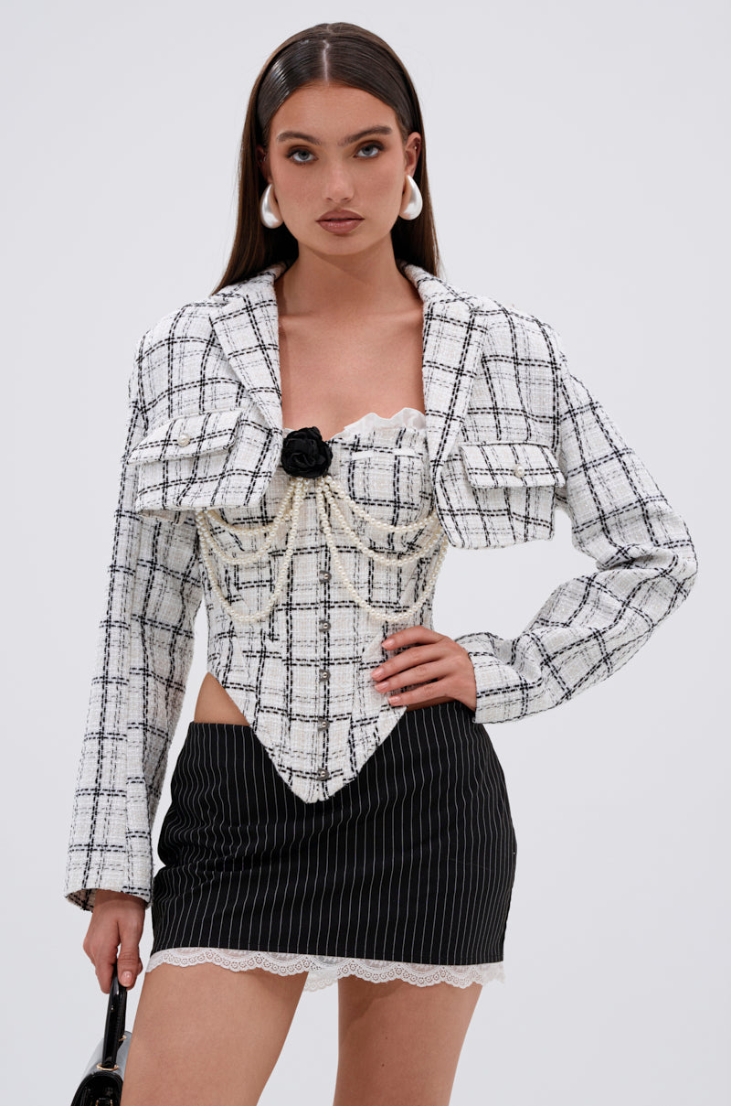Wearing the HEAVEN SENT CROPPED TWEED BLAZER with pearl buttons and decorative pearls, a woman pairs it with a black pinstripe mini skirt featuring lace trim, posing against a plain light background. 0