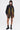 A woman wearing futuristic sunglasses, the MARLEY LACE UP BOMBER with colorful ribbon fringe, black sheer shorts, and black combat boots stands against a plain white background.