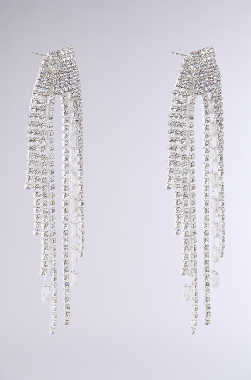 The INTO THE NIGHT BLING EARRINGS feature silver chandelier designs with cascading strands of shimmering rhinestones that create a dazzling effect against a plain background.