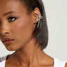 A close-up of an individual with short hair showcases the elegant BOW PLEASE EAR CUFF SET, adorned with rhinestones forming a bow. They wear a white top accented with black ribbons, complemented by bold makeup featuring dark eyeliner and glossy lipstick.