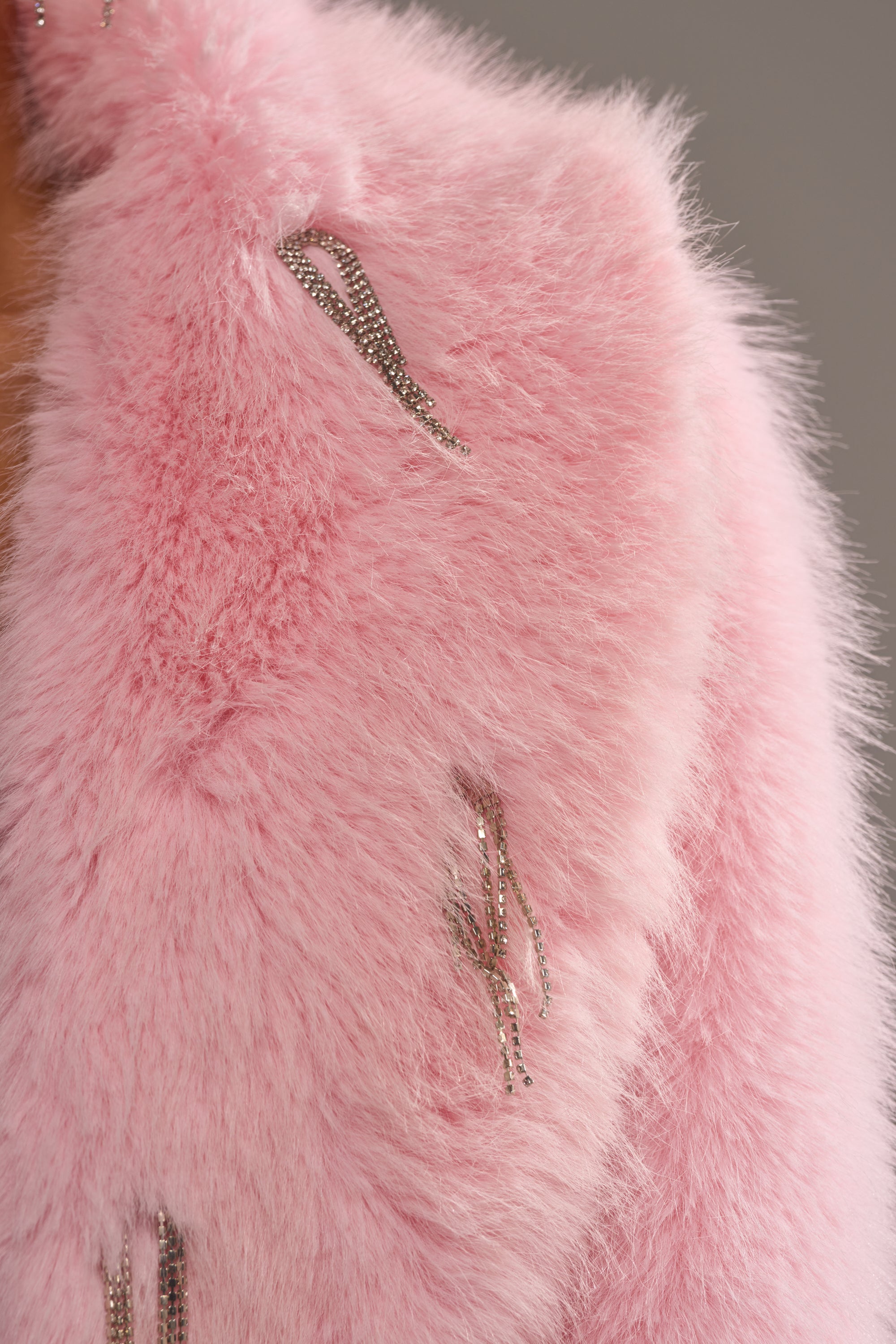 Close-up of the SWEET TALK EMBELLISHED FAUX FUR jacket, featuring soft pastel pink faux fur and shiny silver chain details, set against a neutral background. 7
