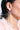 A person wears TULIP TIME EARRING featuring pink petals and a green stem with sparkling rhinestones. Their short dark hair pairs well with the pink fluffy garment, embodying a chic springtime look against the soft light background.