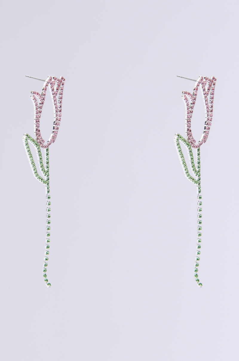Introducing the TULIP TIME EARRING, a chic spring accessory with flower-like design. Pink gemstones as blooms sparkle, and green rhinestones form glistening stems and leaves, all elegantly set against a white backdrop.