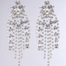 The CALL ME QUEEN EARRING features a dazzling pair of faux silver chandelier earrings embellished with multiple strands of shimmering rhinestone fringe, designed to capture light and offer an elegant, glamorous look against a subtle gray background.