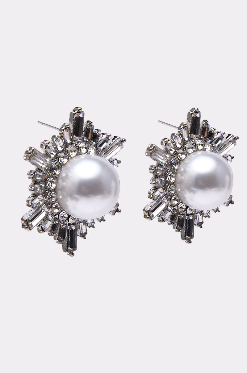 The TAY EARRING features large central pearls accented with radiant rhinestones in a starburst design, set against a plain white background for a glamorous touch.