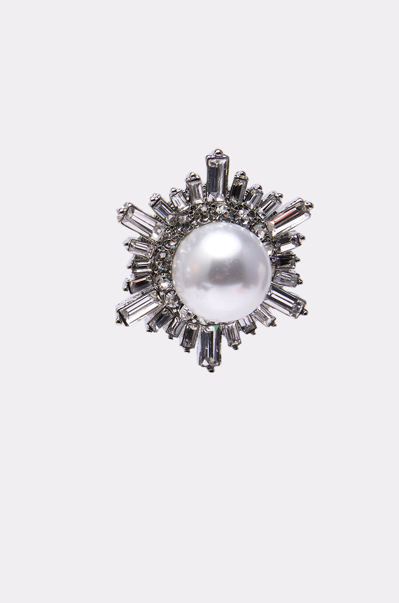 The TAY EARRING showcases a large central pearl accented by a starburst design of silver baguette crystals and delicate rhinestones, set against a light gray background.