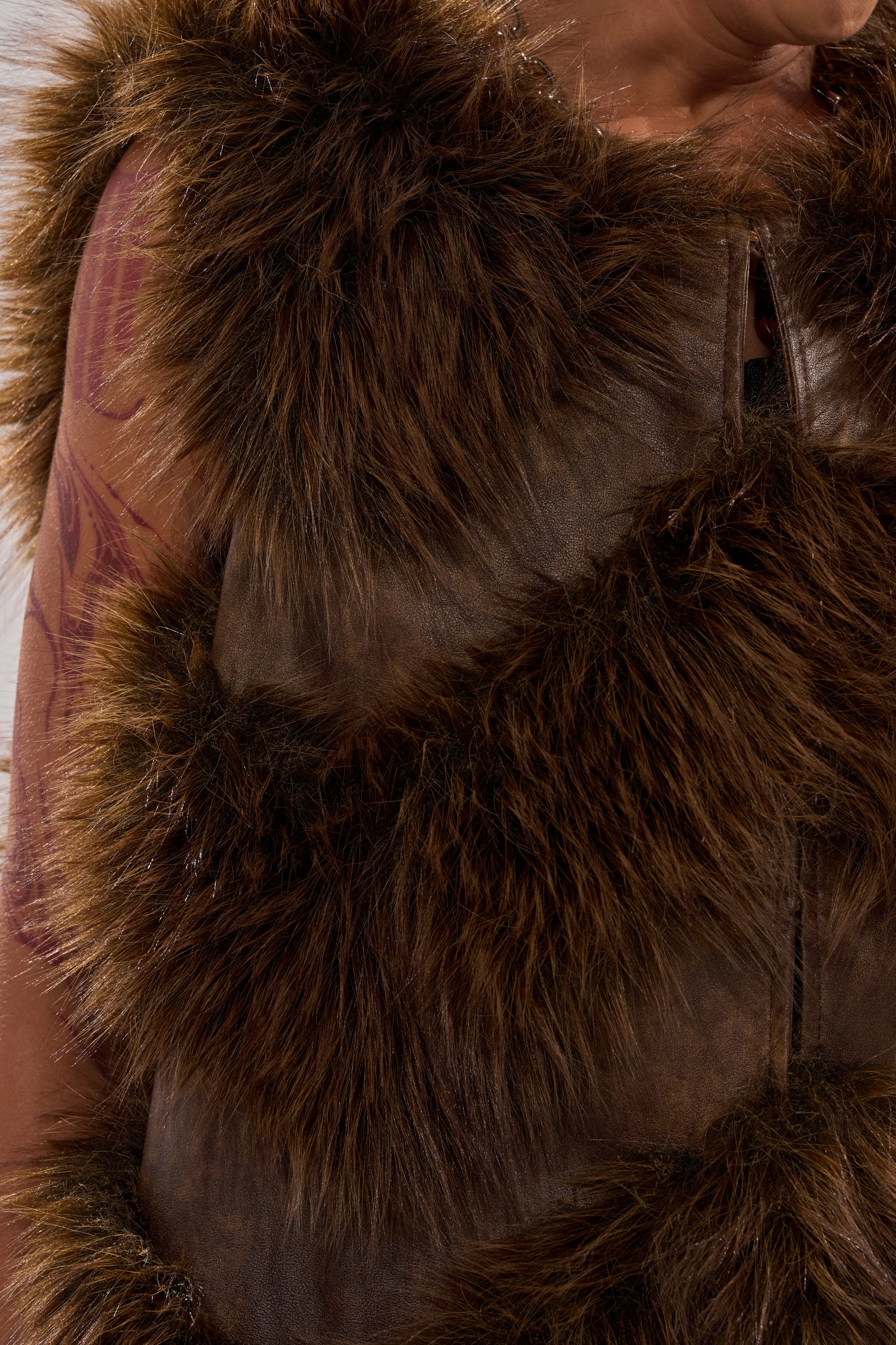 A close-up of a person wearing the CAN'T BE BOTHERED PANELED FUR VEST, showcasing its chevron design, textured faux fur, and part of a tattooed arm.