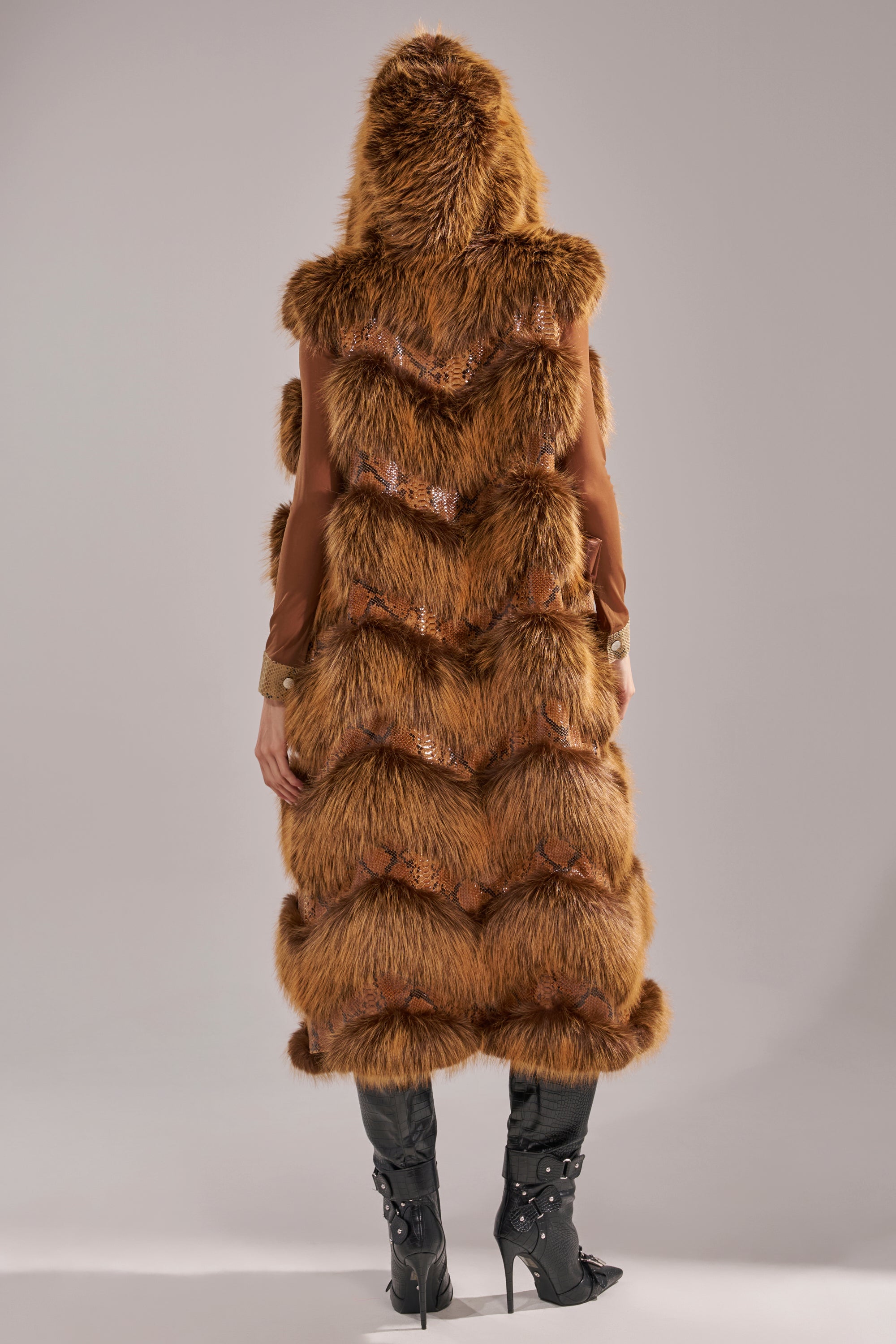 A person stands with their back to the camera, wearing the GOOD OMEN FUR TRIM VEST paired with heeled black boots. The vest features a textured faux fur finish and is photographed against a plain neutral background. 9