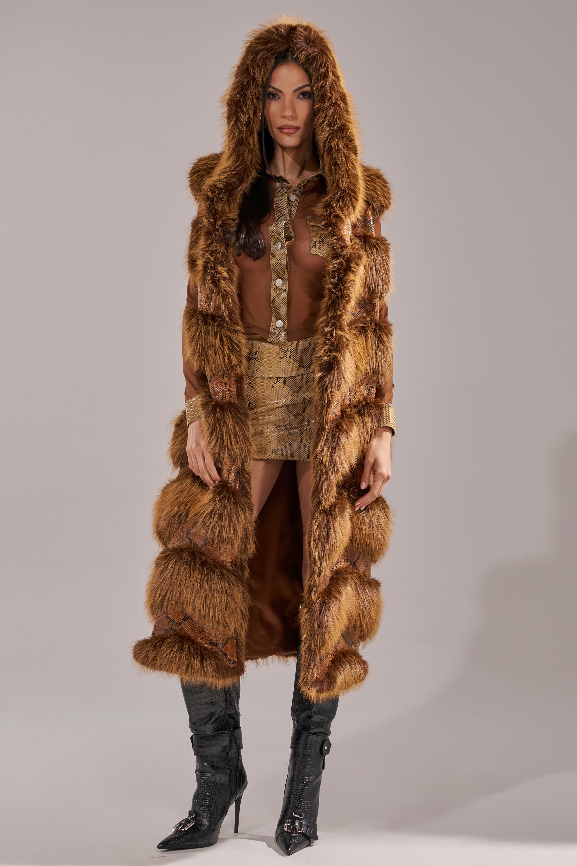A woman stands facing forward against a plain gray background, wearing the GOOD OMEN FUR TRIM VEST over a shiny gold dress and knee-high black boots. 4