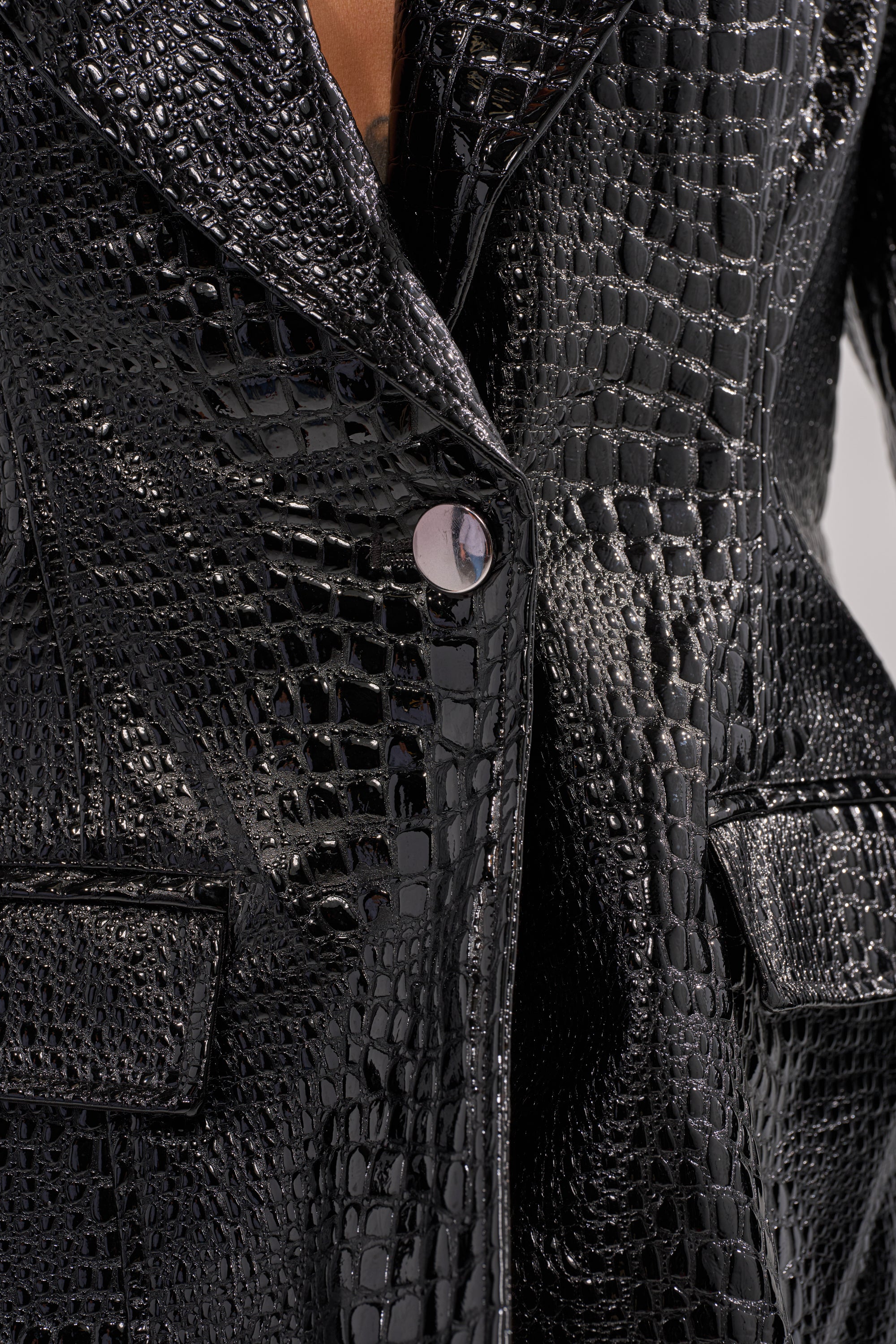 The FOR THE DRAMA CROC BLAZER showcases shiny black faux patent leather with a crocodile print, two front pockets, and a central single round button fastening.