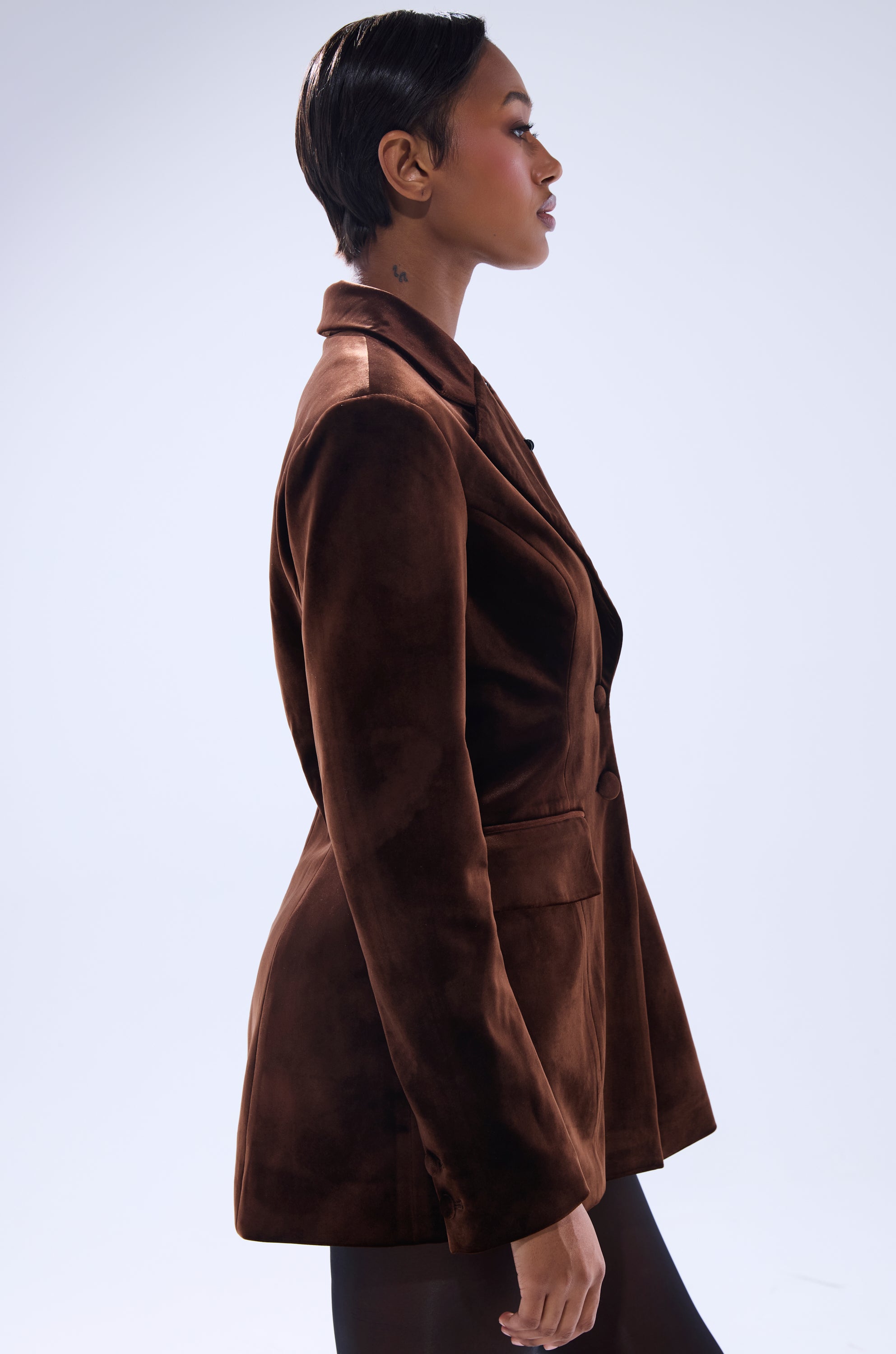 A woman with short dark hair wears the SUNDAY VELVET BLAZER WITH REMOVABLE FUR COLLAR, standing in profile against a plain light background.
