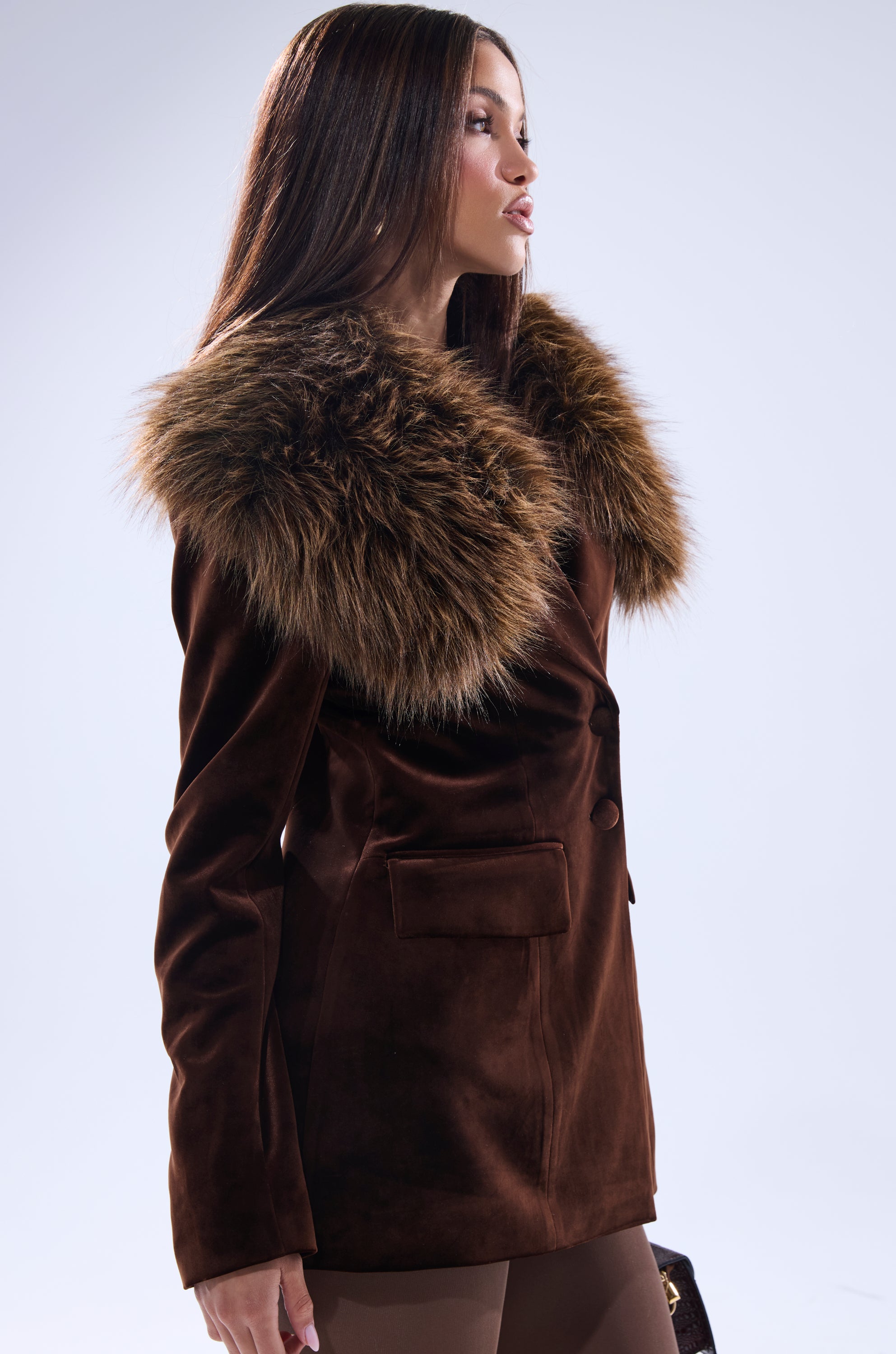 A woman in profile looks to the side against a plain light background, wearing the SUNDAY VELVET BLAZER WITH REMOVABLE FUR COLLAR.