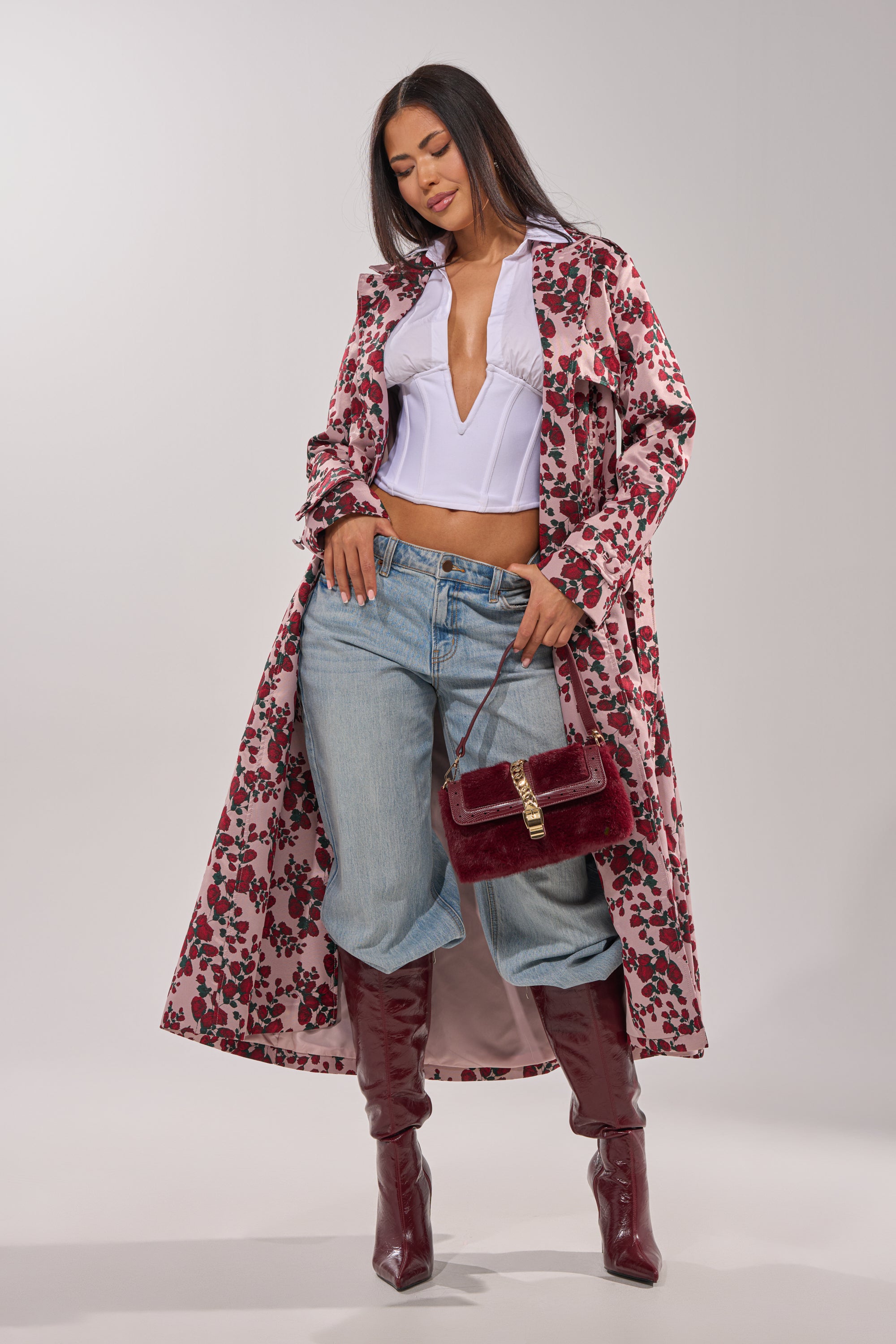 A woman poses in the BUY ME ROSES JACQUARD TRENCH over a white blouse and blue jeans, styled with knee-high burgundy boots and a matching handbag, standing against a plain background. 3