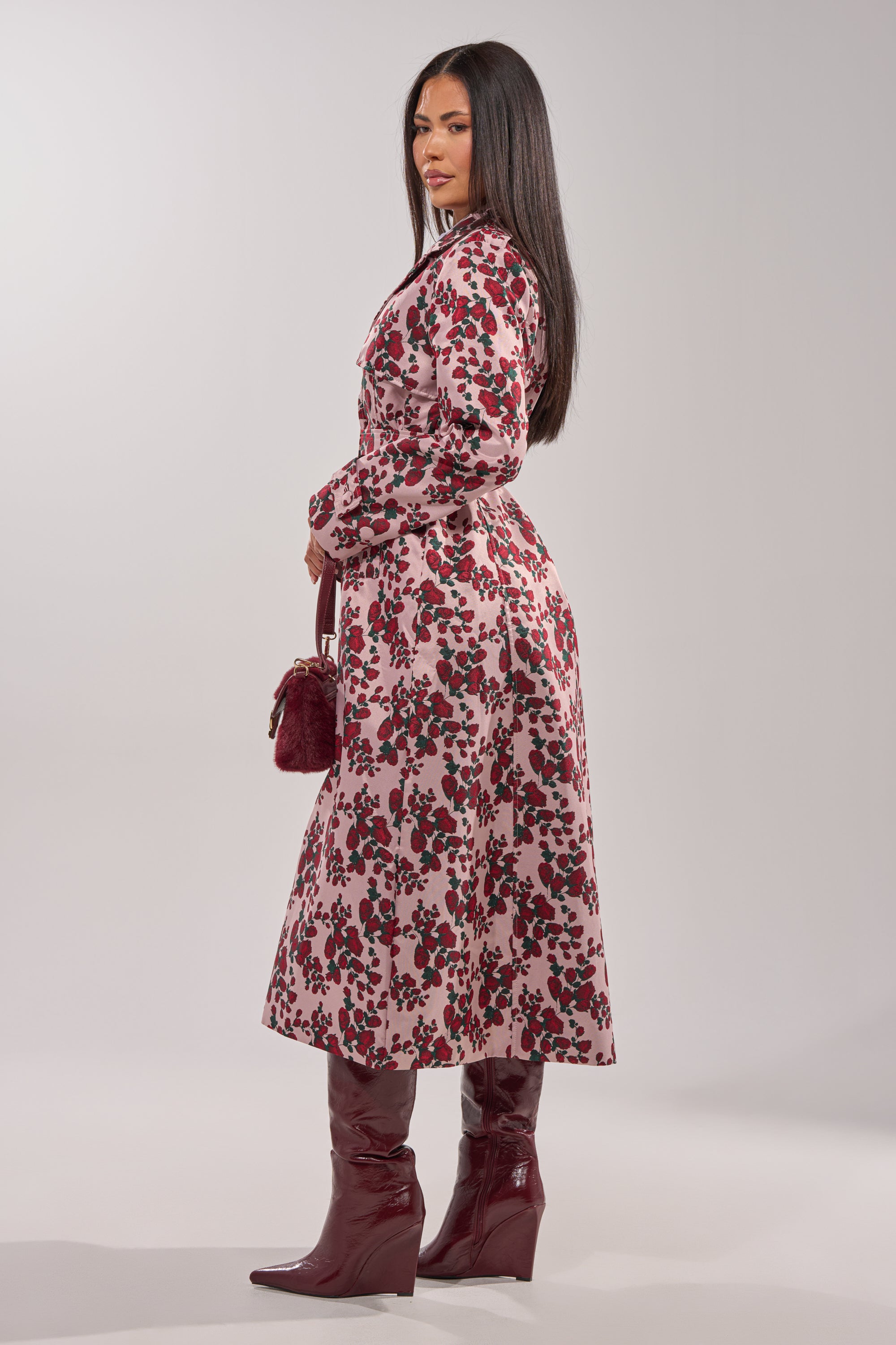 A woman with long dark hair wears the BUY ME ROSES JACQUARD TRENCH and matches it with red boots and a small red handbag, posing against a plain light background. 8