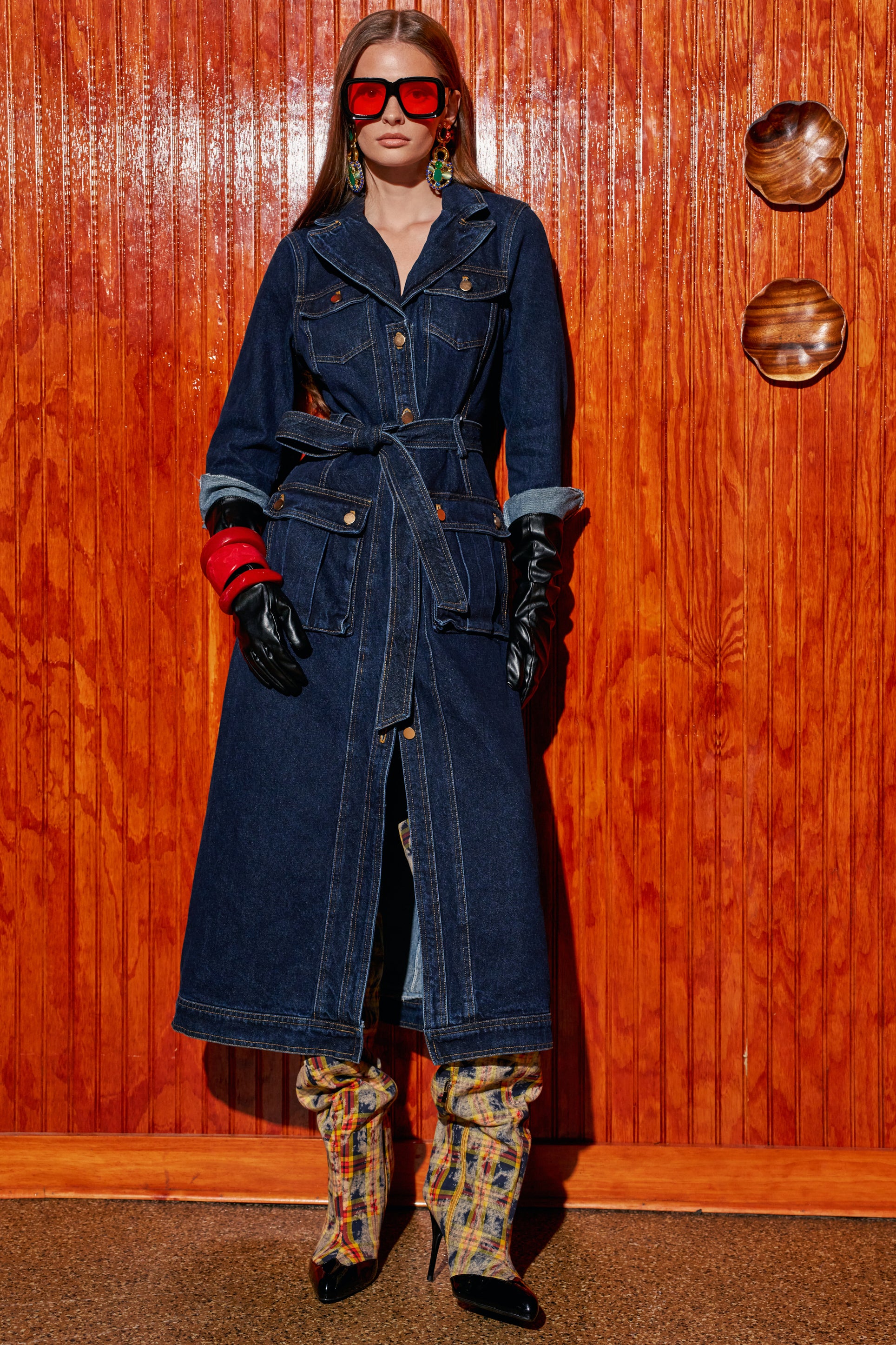 A person wears a CAMILLA DENIM TRENCH IN DARK BLUE with a waist tie, black leather gloves, and patterned high-heeled boots in a piece of streetwear styling.