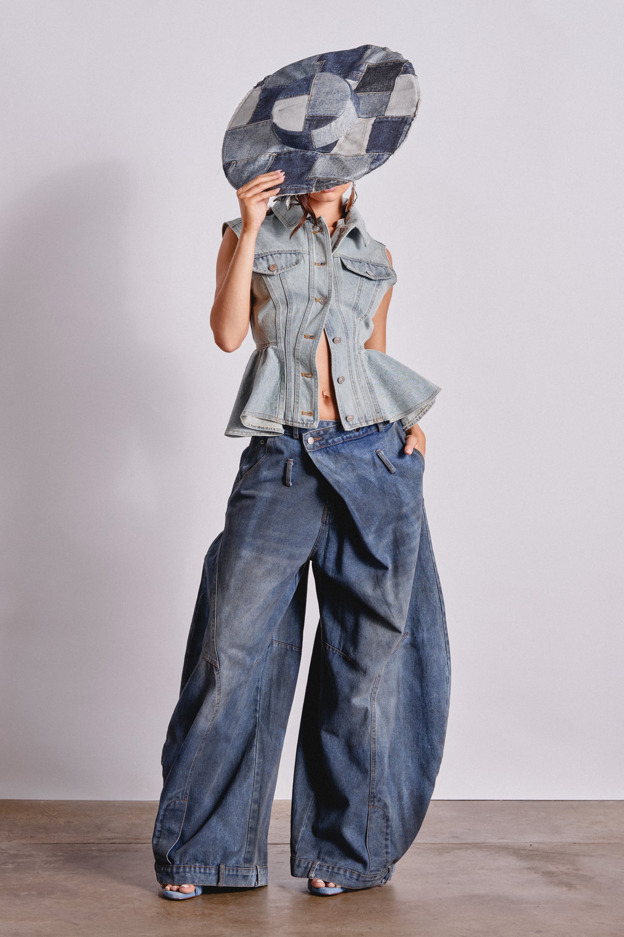 Wearing the FORGET ABOUT YOU PEPLUM DENIM VEST and wide-leg baggy jeans, a person holds a large patchwork denim hat in front of their face, posing against a plain background. 4
