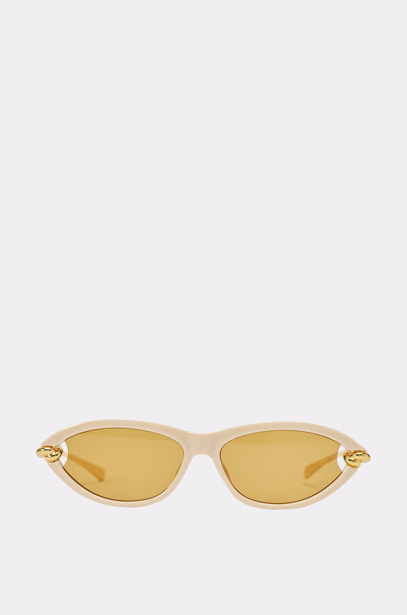 The GOLDEN HOUR CAT HOUR SUNGLASSES feature a beige cat-eye frame with gold-tinted lenses and small gold decorative accents on each temple—these chic vacation sunglasses are displayed against a plain light gray background.