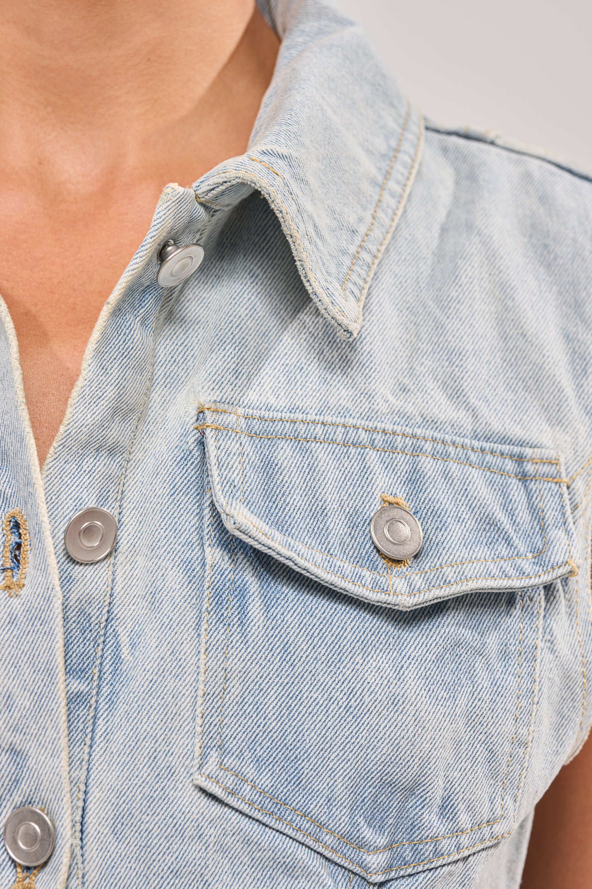 Close-up of a person in a light wash denim shirt with metal snaps and a chest pocket, styled under the HIGH LOW DENIM VEST. The shirt’s open collar reveals part of the neck and chest, complementing the layered denim look. 6
